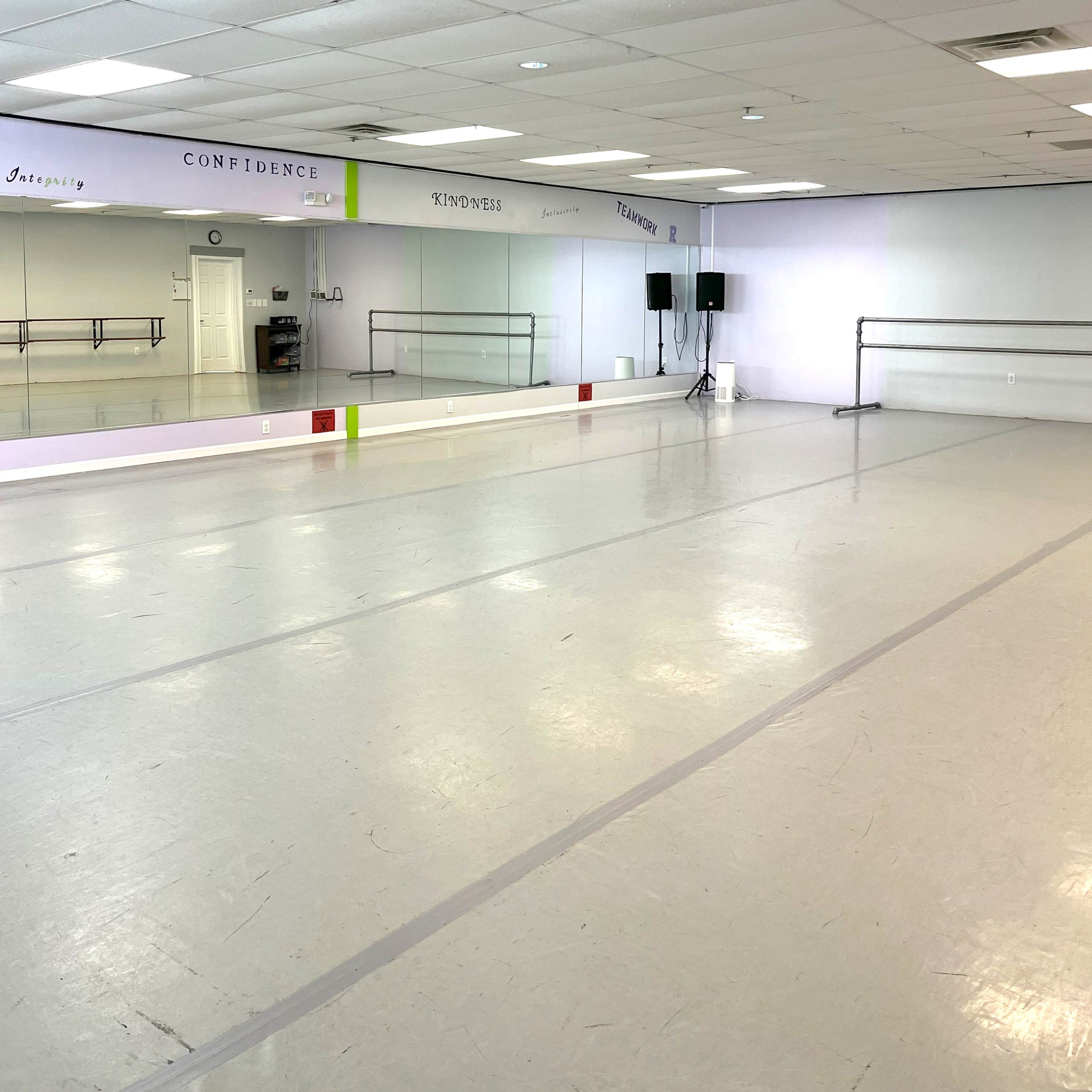 A spacious dance studio with a mirrored wall, wooden ballet bars, and motivational words painted on the walls.