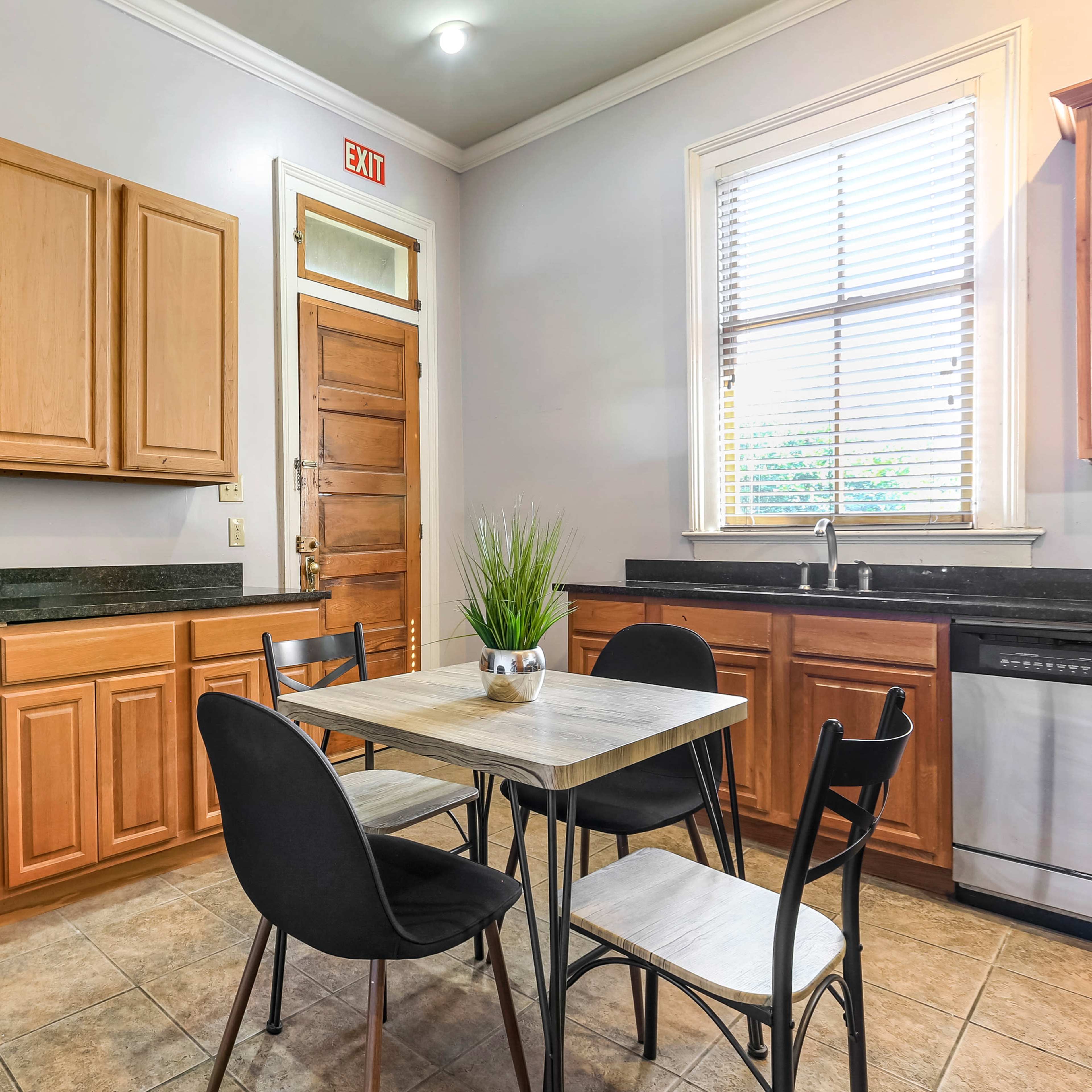 A compact kitchen features wooden cabinets, a black refrigerator, a dishwasher, and a small dining table with four chairs.