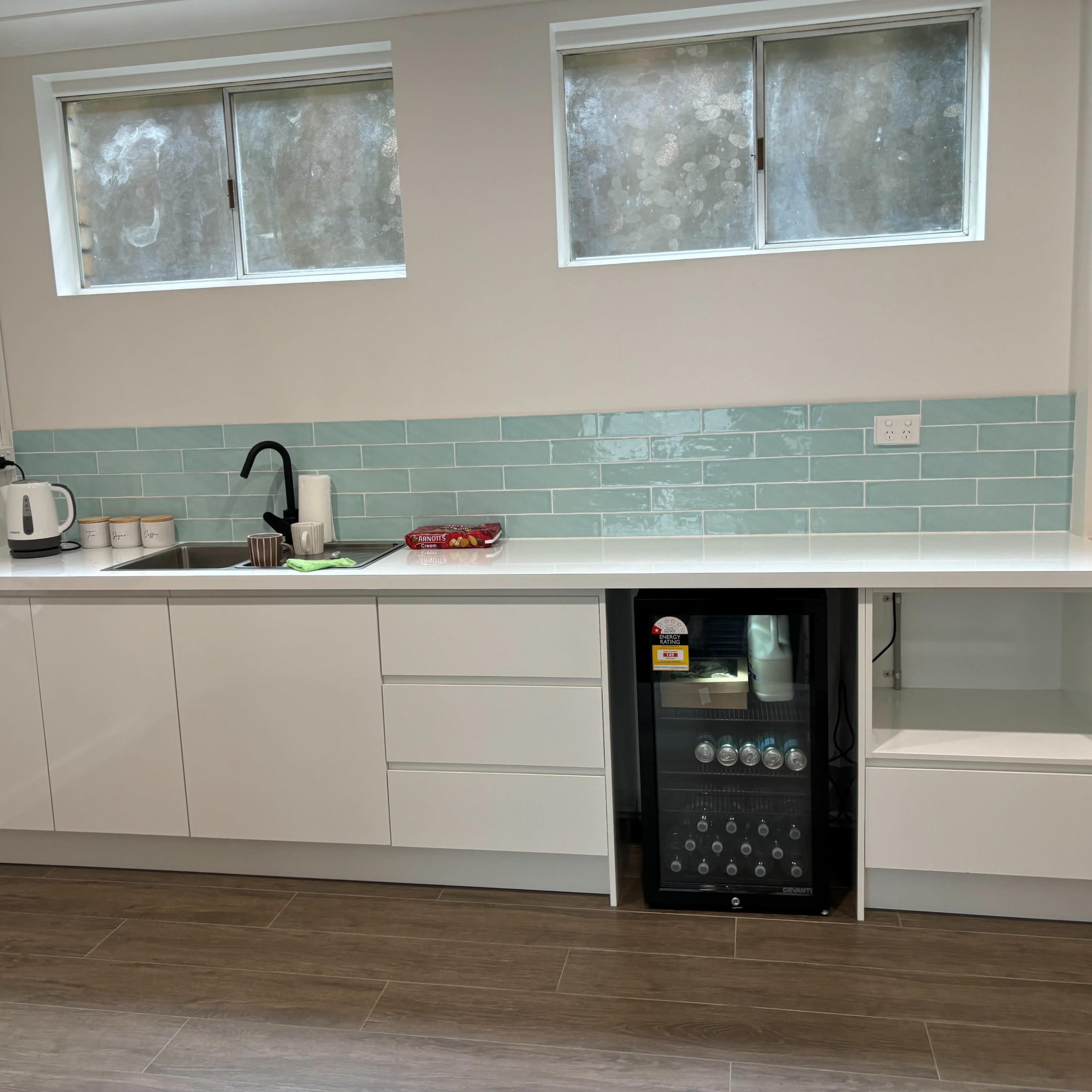 A modern kitchen with white cabinetry, a light turquoise tiled backsplash, and a small beverage fridge beside the sink.