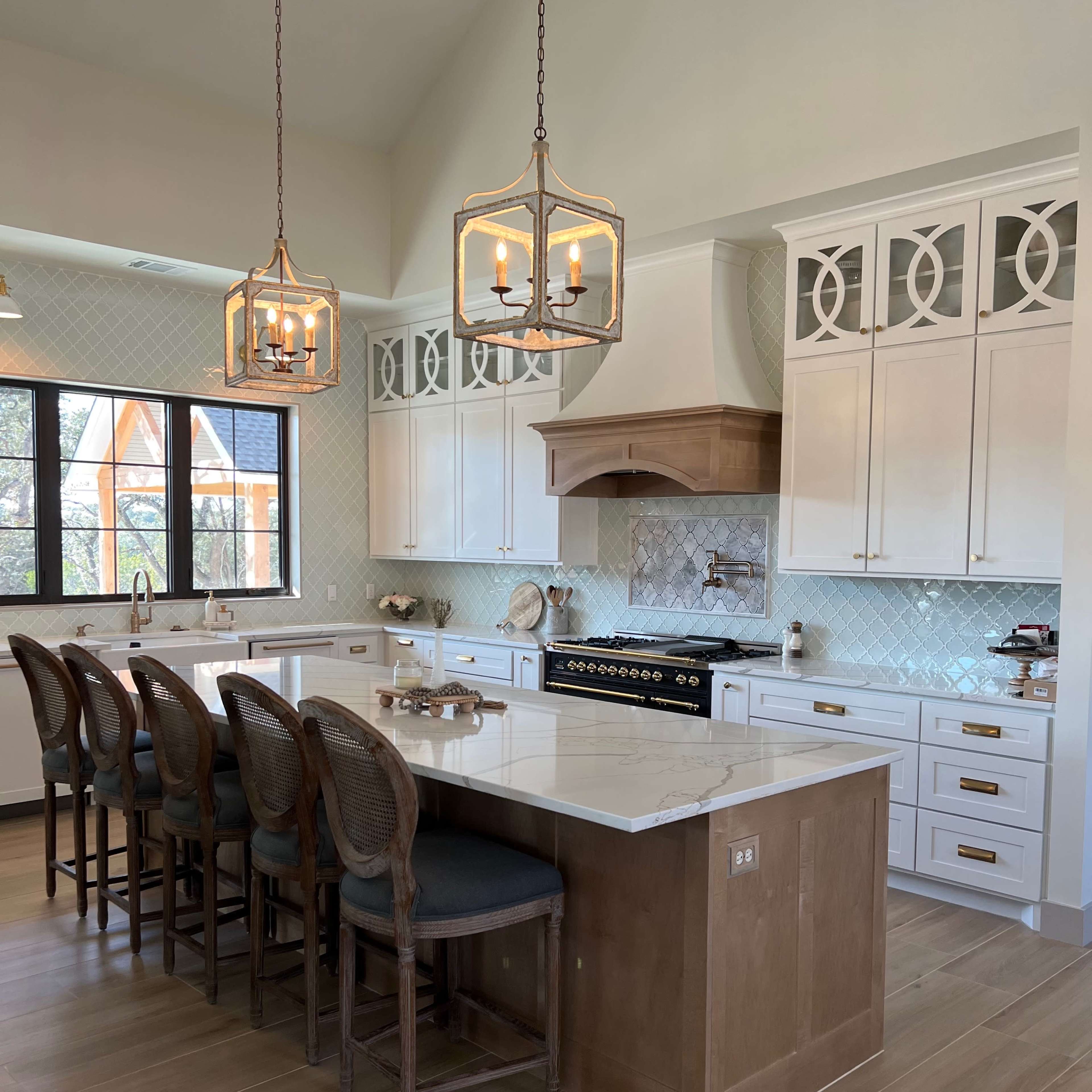 A modern kitchen with a large island, seating for several people, white cabinets, and pendant lighting.
