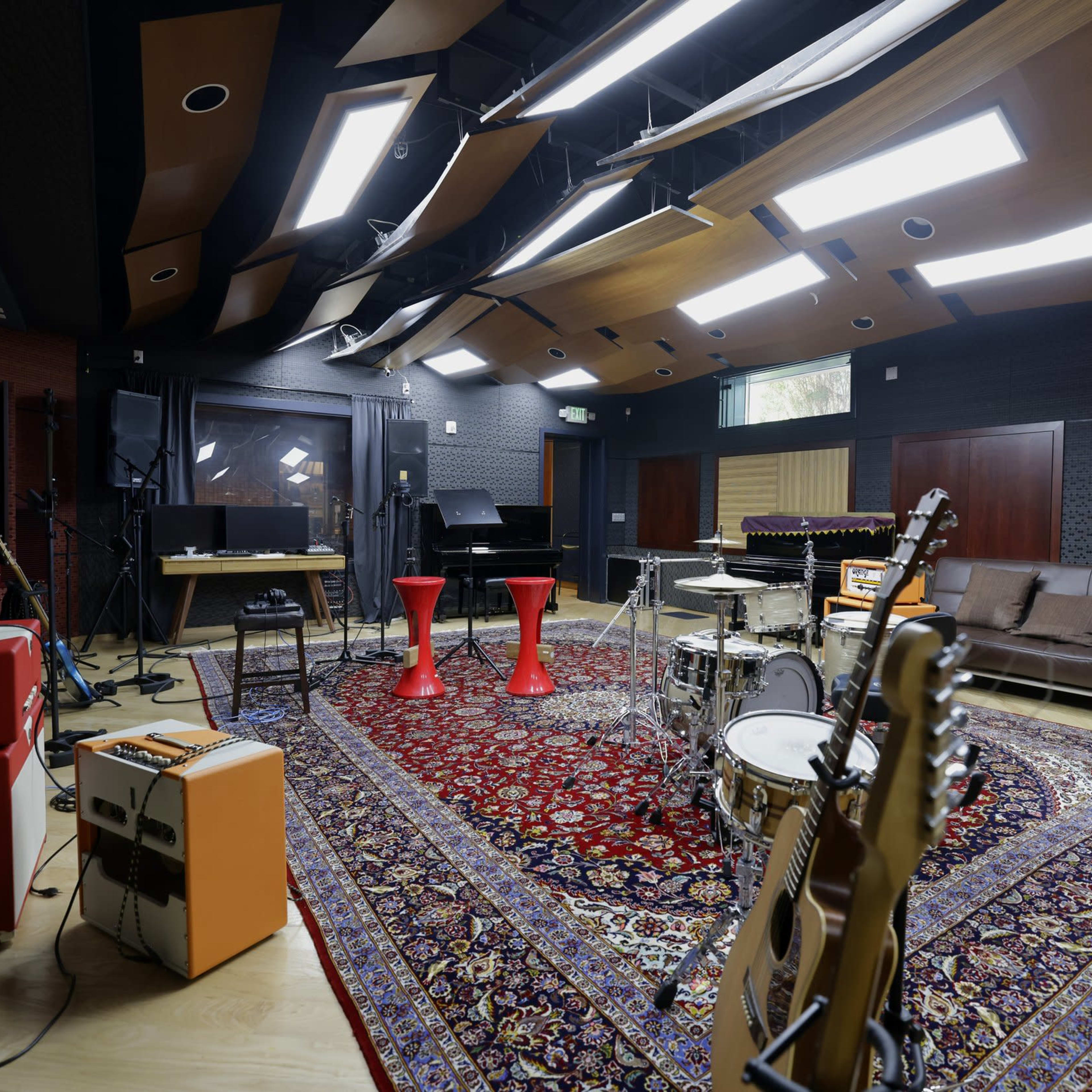 A music studio with various instruments, a sofa, and red stools arranged on a patterned rug.