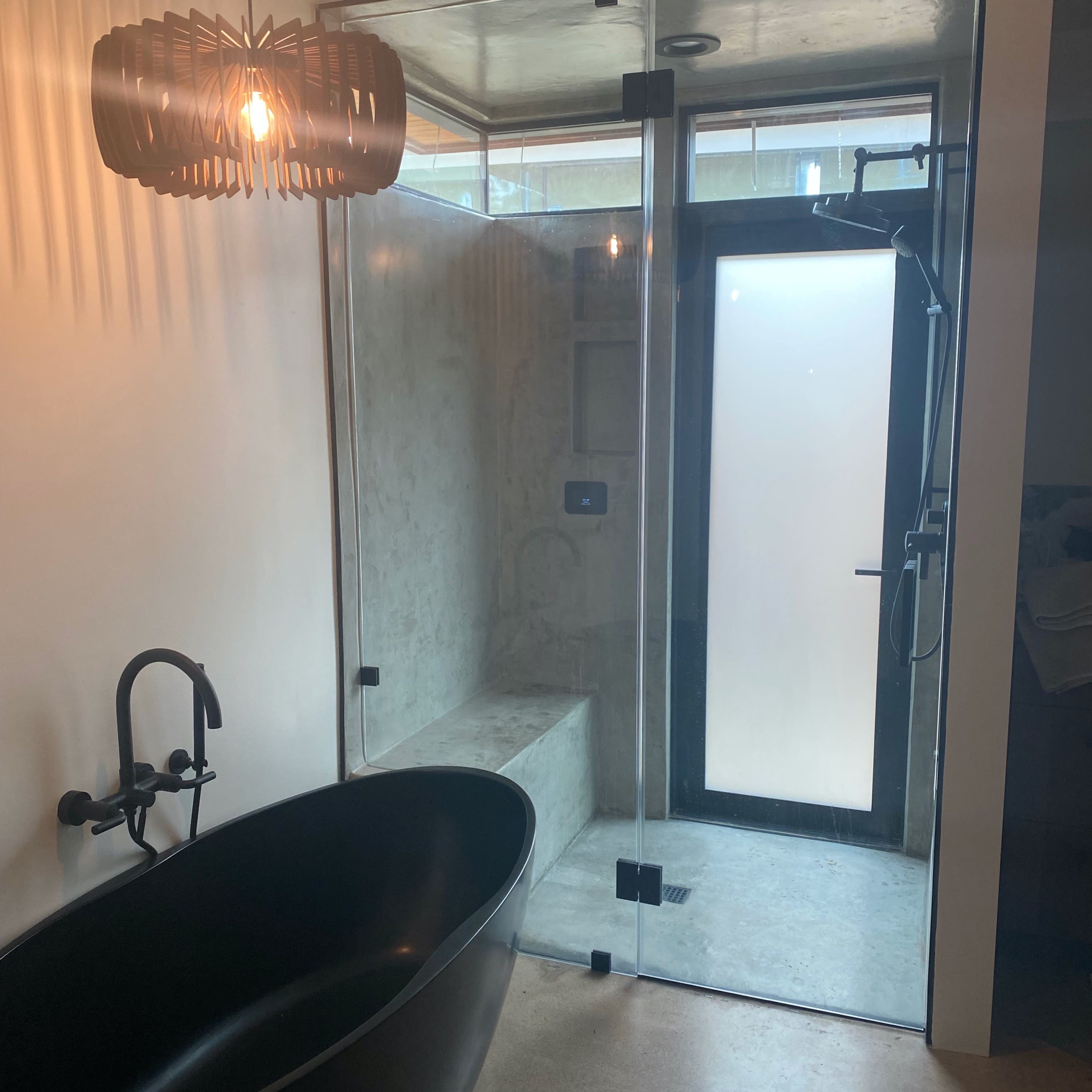 A modern bathroom featuring a glass shower enclosure, a freestanding black bathtub, and a pendant light fixture.