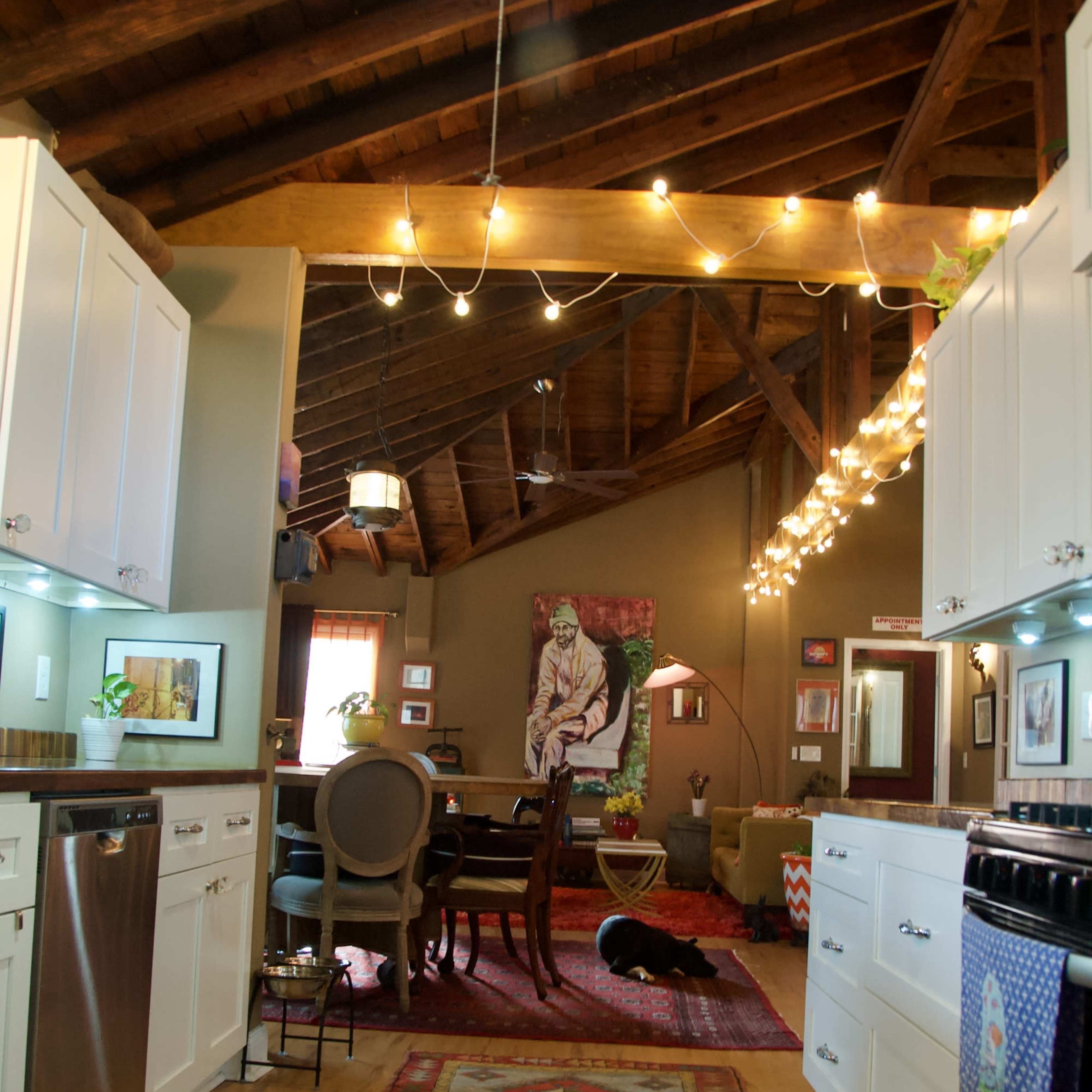 A spacious kitchen and dining area featuring wooden beams, white cabinetry, a large rug, and a pet dog lying on the floor.