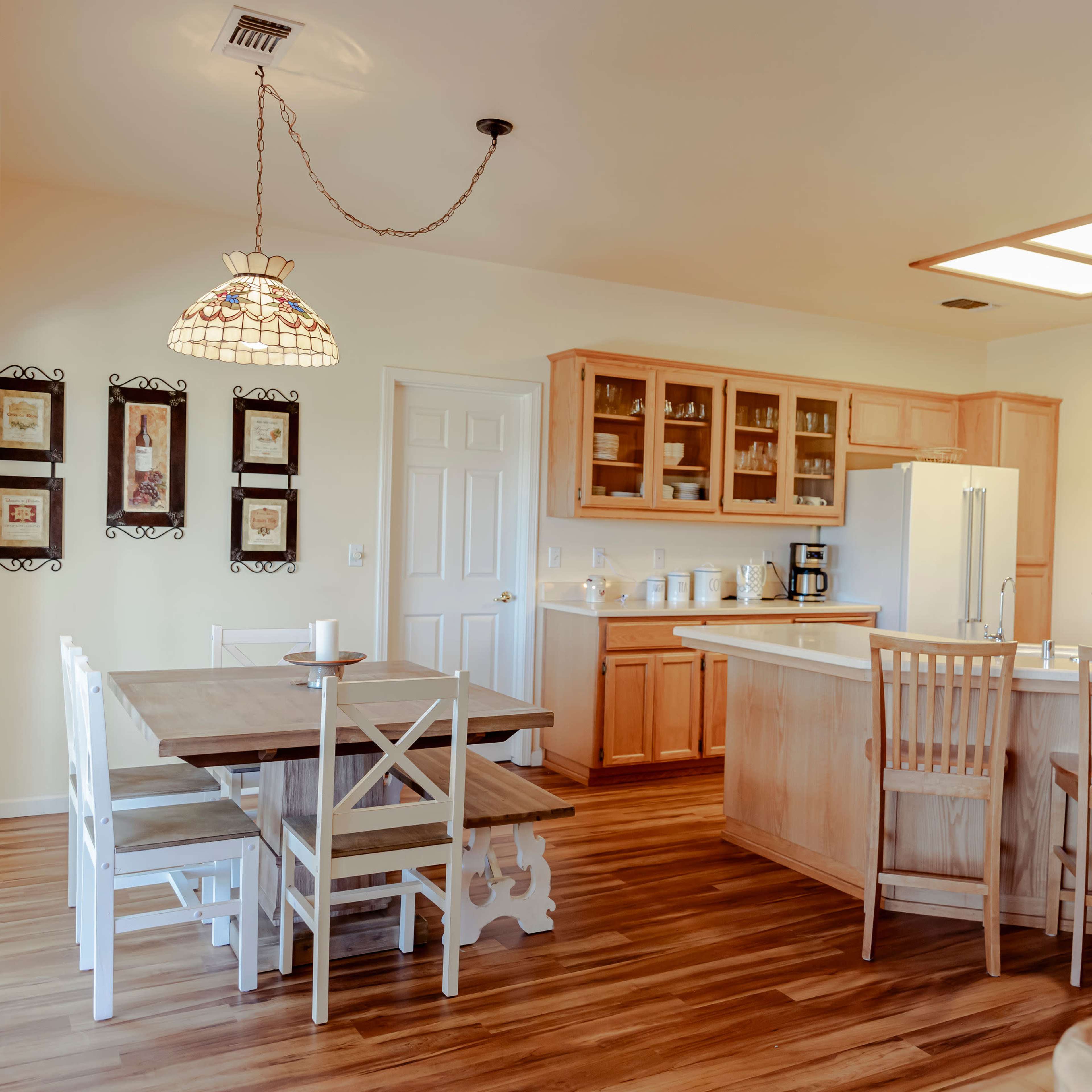 A modern kitchen and dining area with wooden cabinets, a central island, a large table with white chairs, and a pendant light.