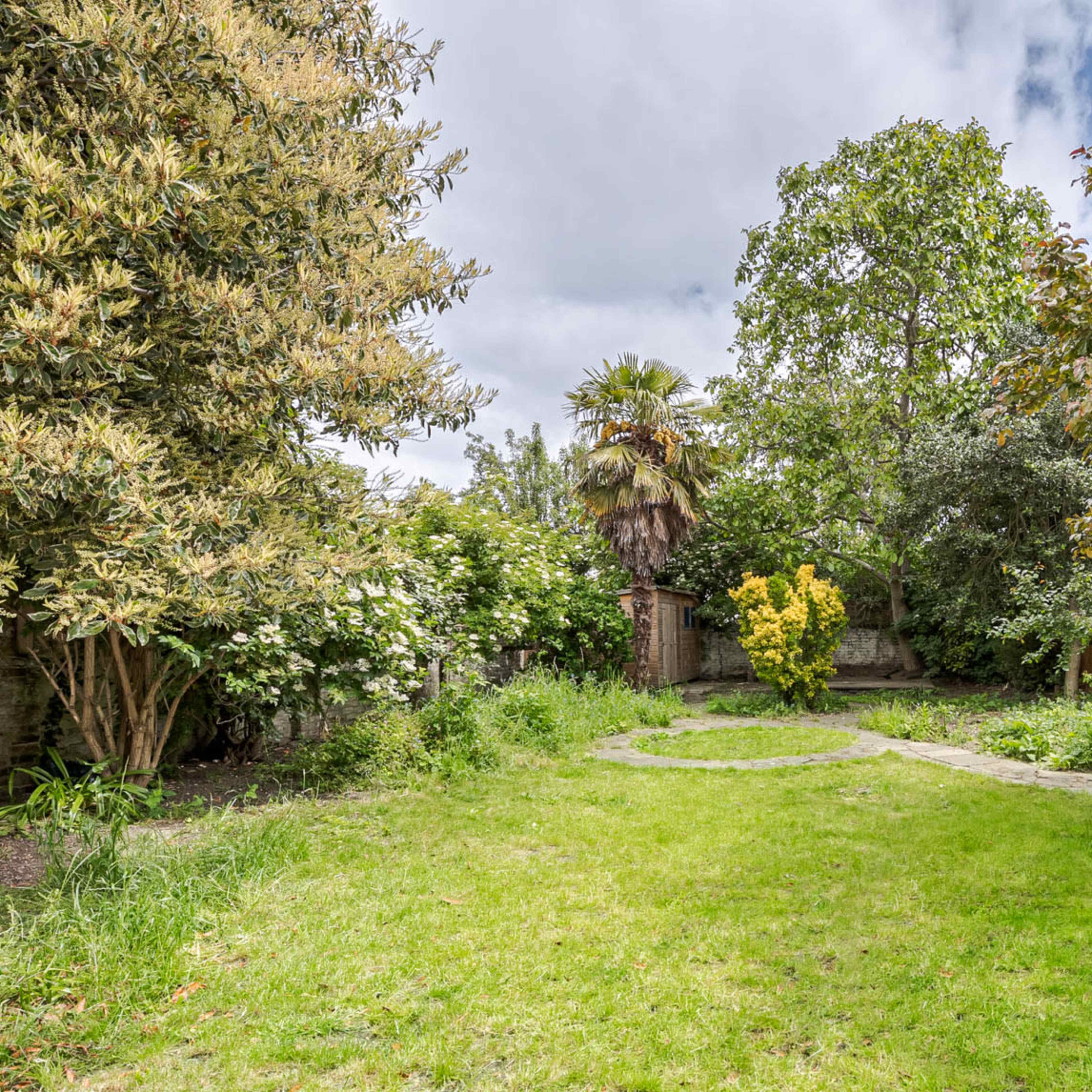 A spacious garden with a circular stone path, surrounded by various trees and shrubs.