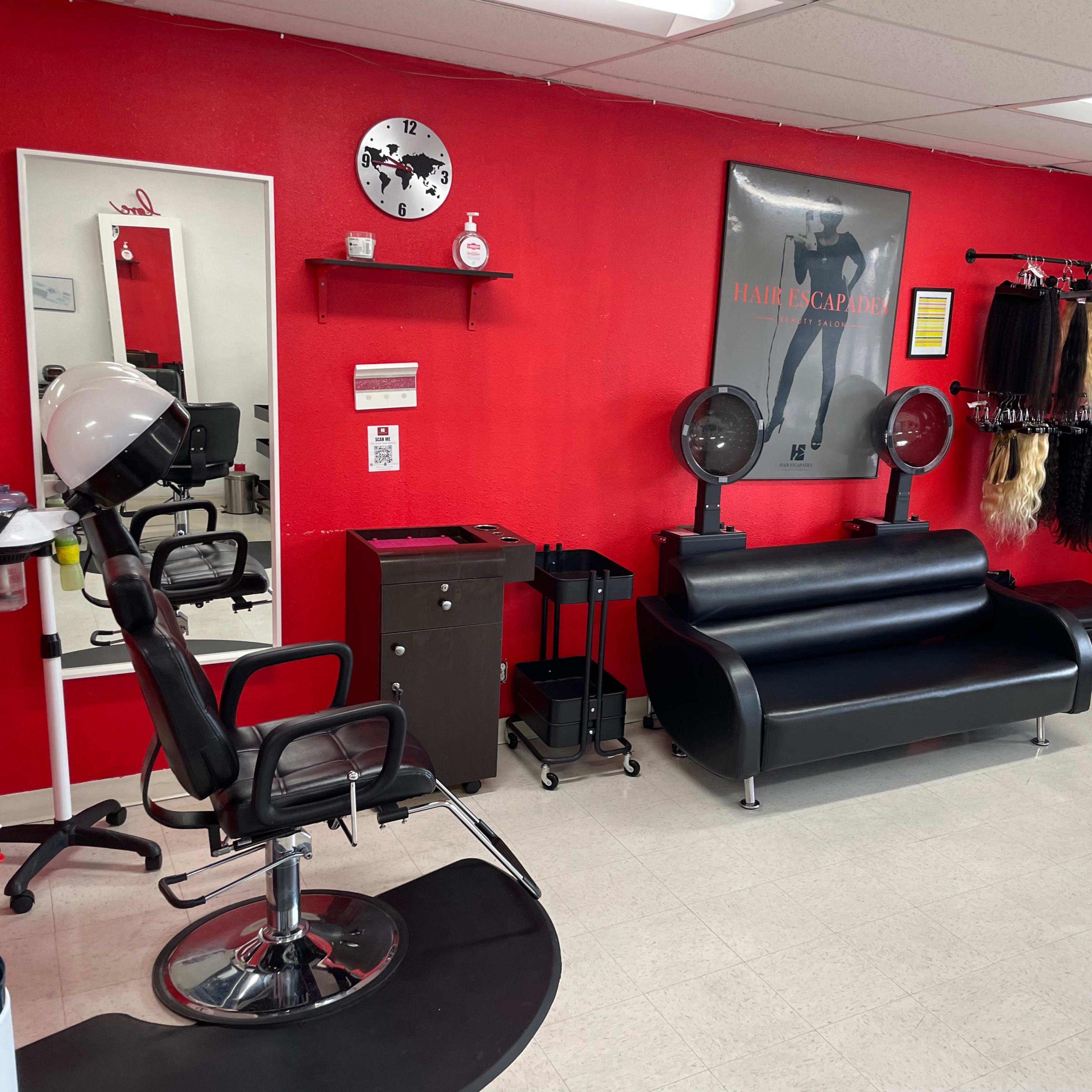 A hair salon featuring a black leather couch, styling chair, mirror, and various hair products displayed against a red wall.
