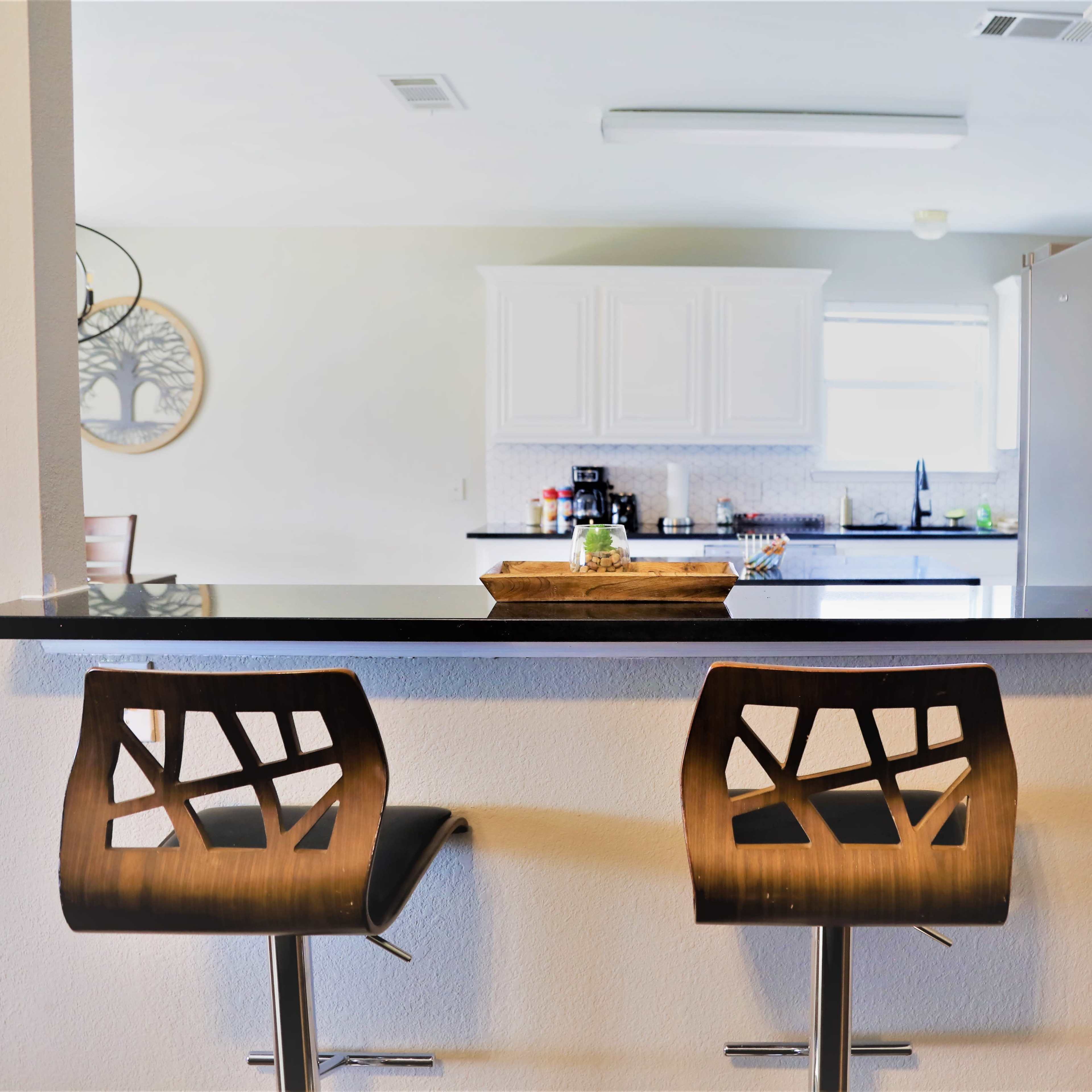 A kitchen with a bar area featuring two modern chairs and a countertop that overlooks the cooking space.