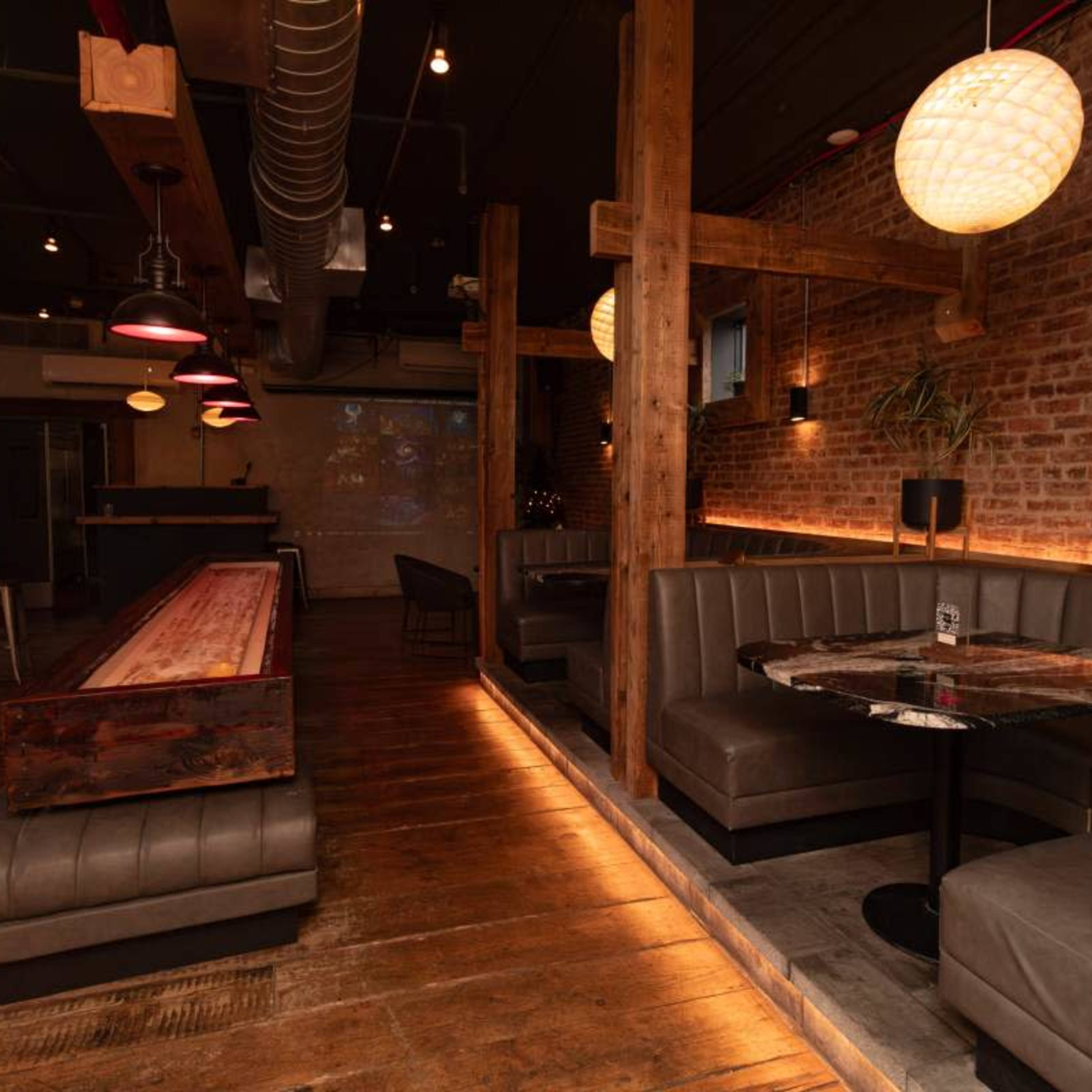 A modern interior of a restaurant featuring wooden beams, brick walls, and booth seating with a bar area in the background.
