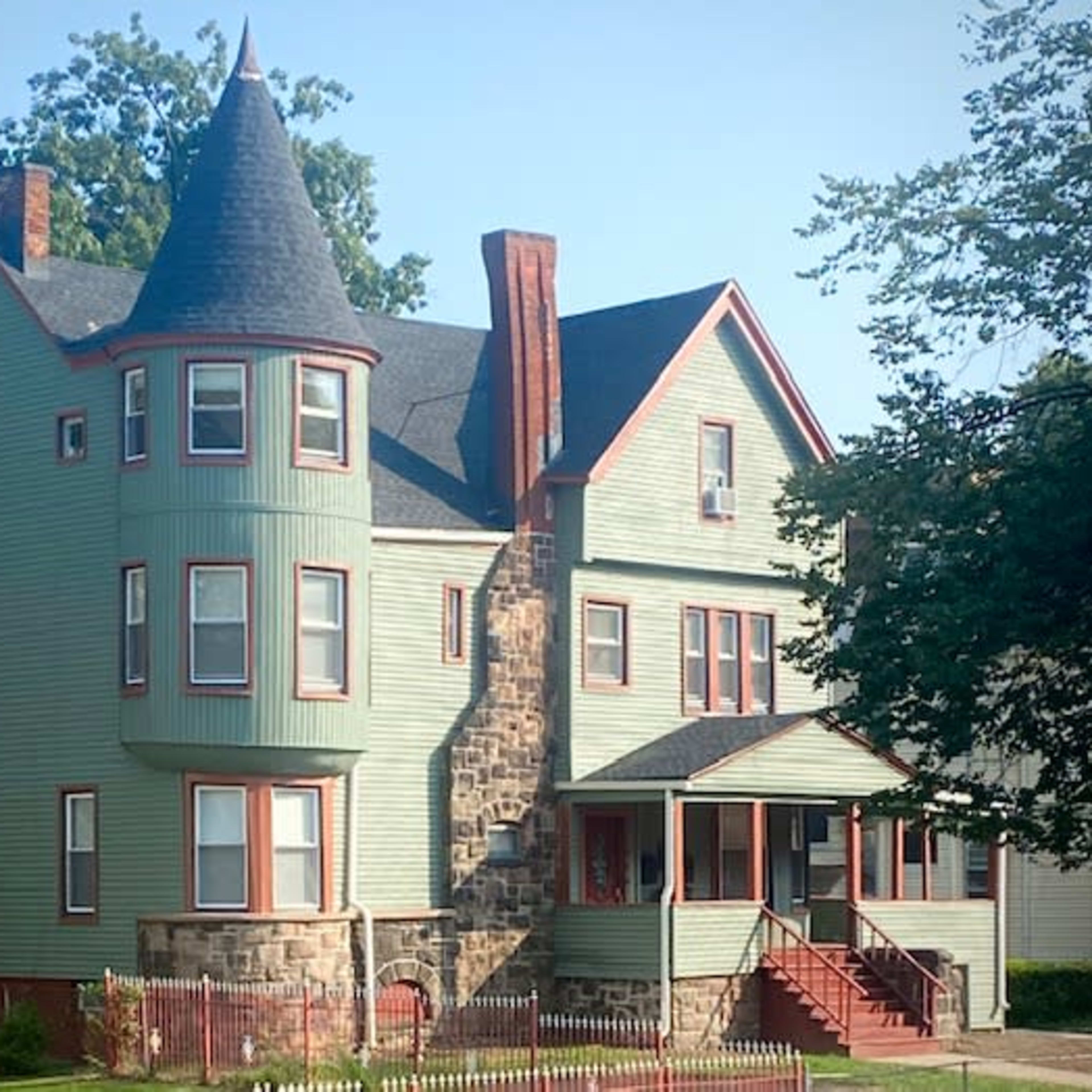 A large, multi-story house featuring a turret, green siding, and a front porch with steps leading up to it.