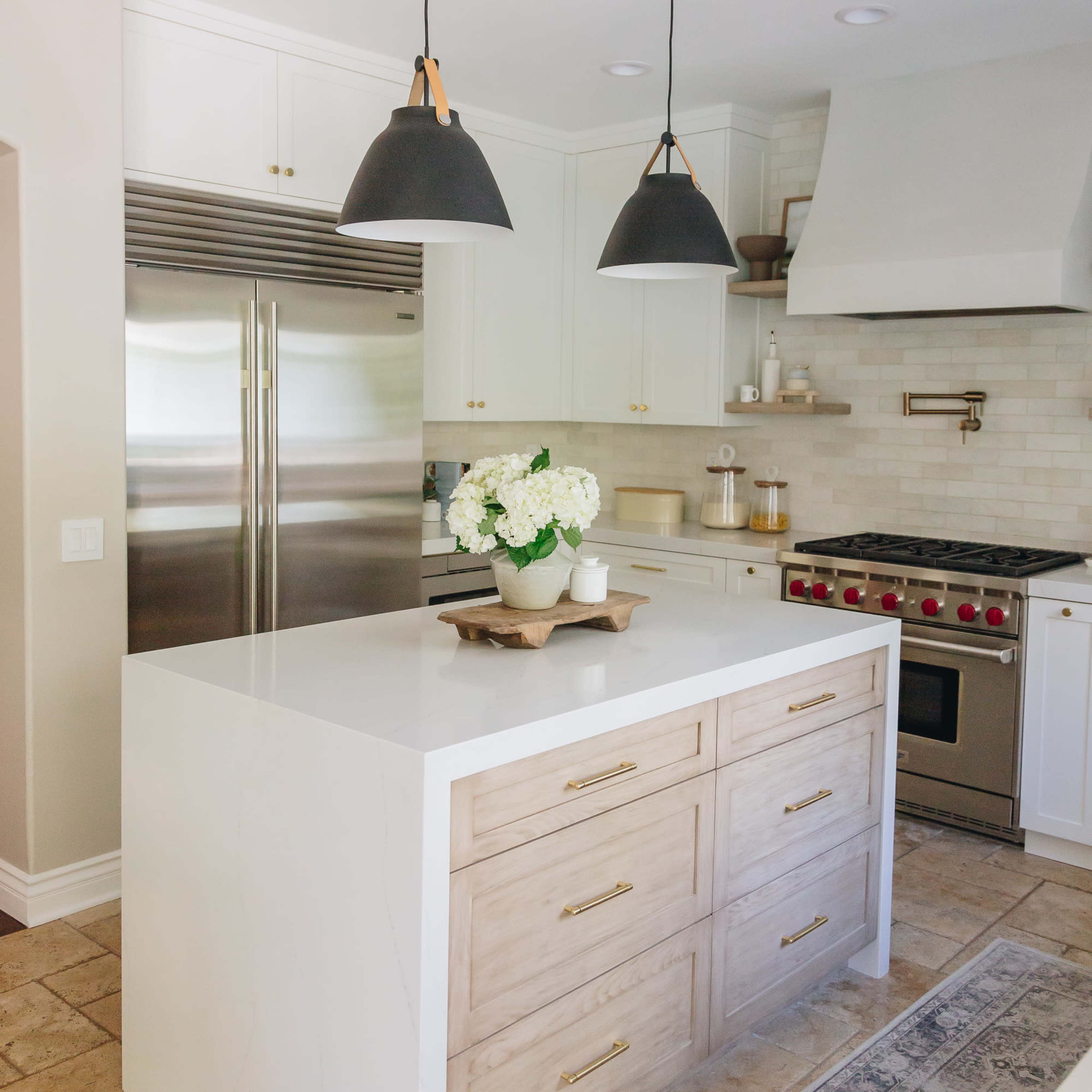 The kitchen features a central island with wooden drawers, stainless steel appliances, and black pendant lights above, complemented by a bouquet of flowers on the countertop.