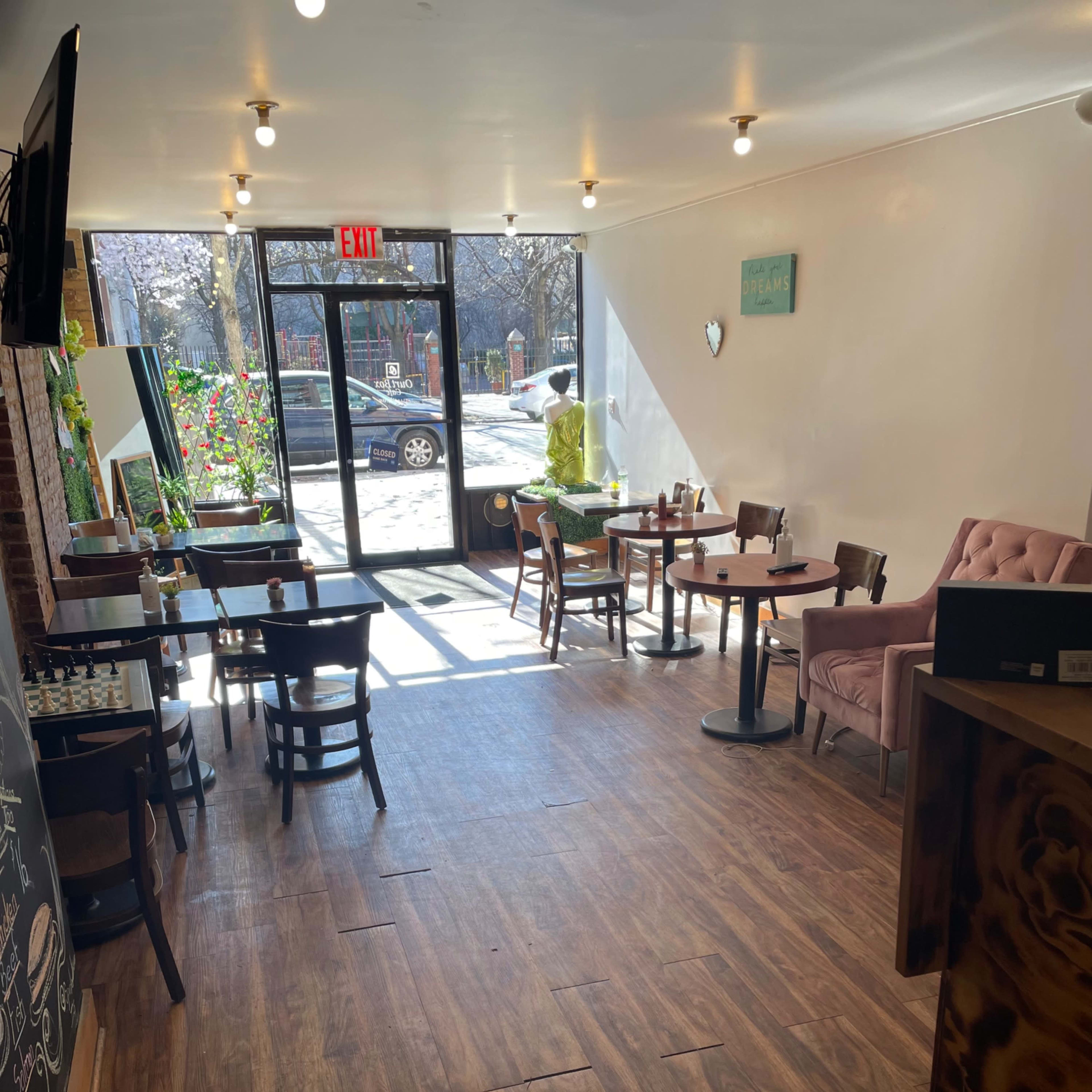 A cozy café interior with wooden flooring, several tables and chairs, and large windows letting in natural light.