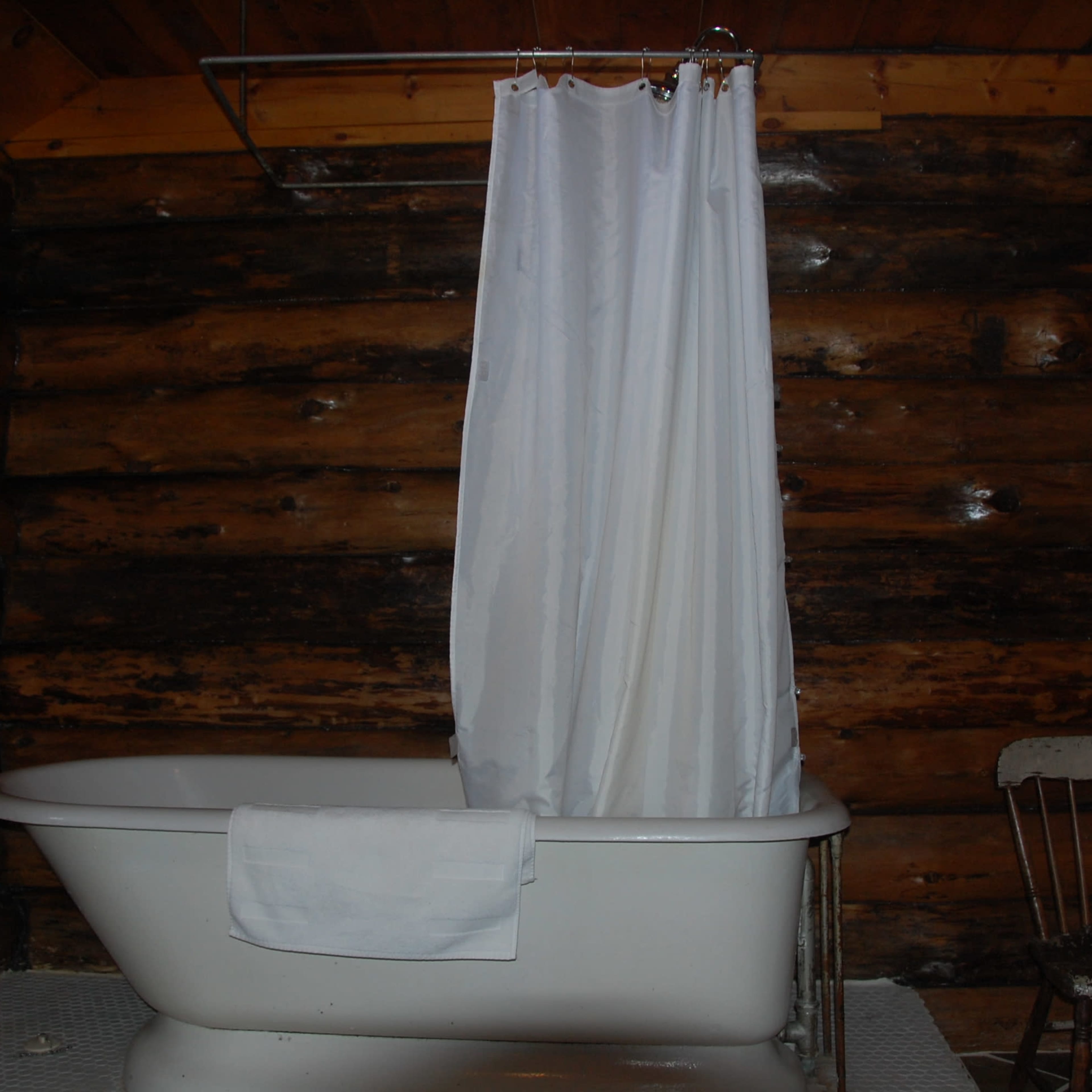 A vintage bathtub with a white shower curtain in a wooden cabin bathroom.