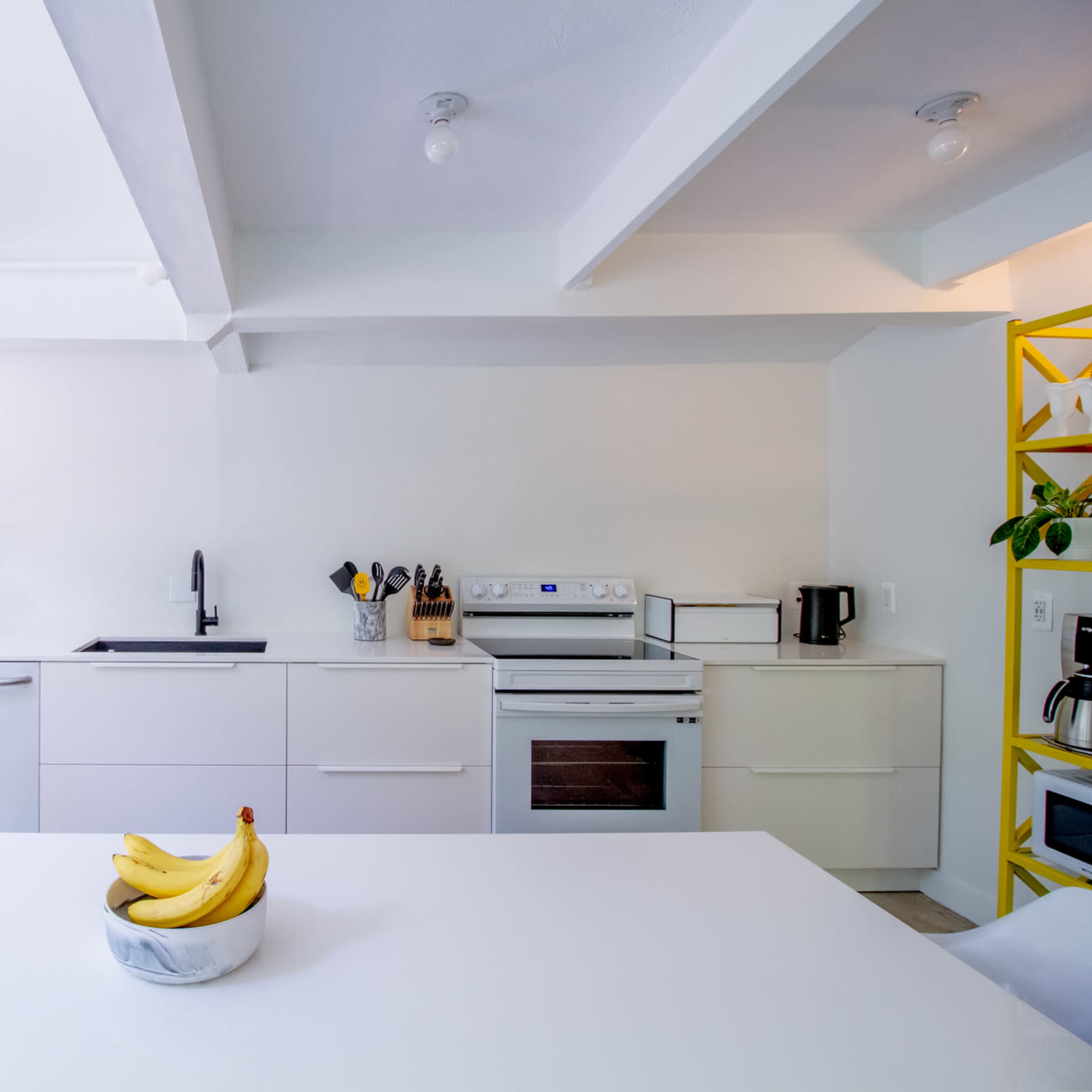 A modern kitchen features a white color scheme, sleek cabinetry, and a central island with a bowl of bananas.
