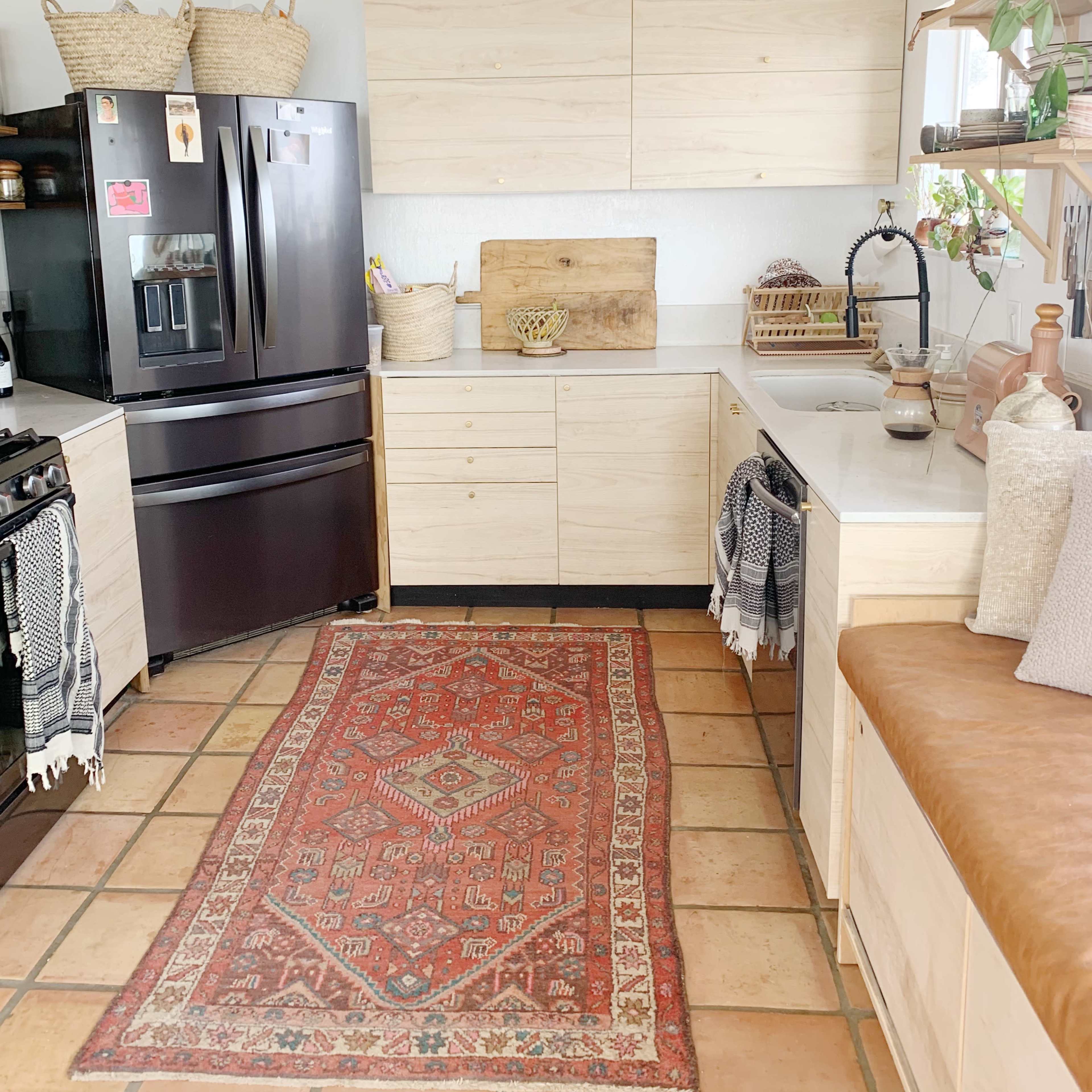 A modern kitchen features wooden cabinetry, a black refrigerator, a tile floor, and a red patterned rug in front of a sink.