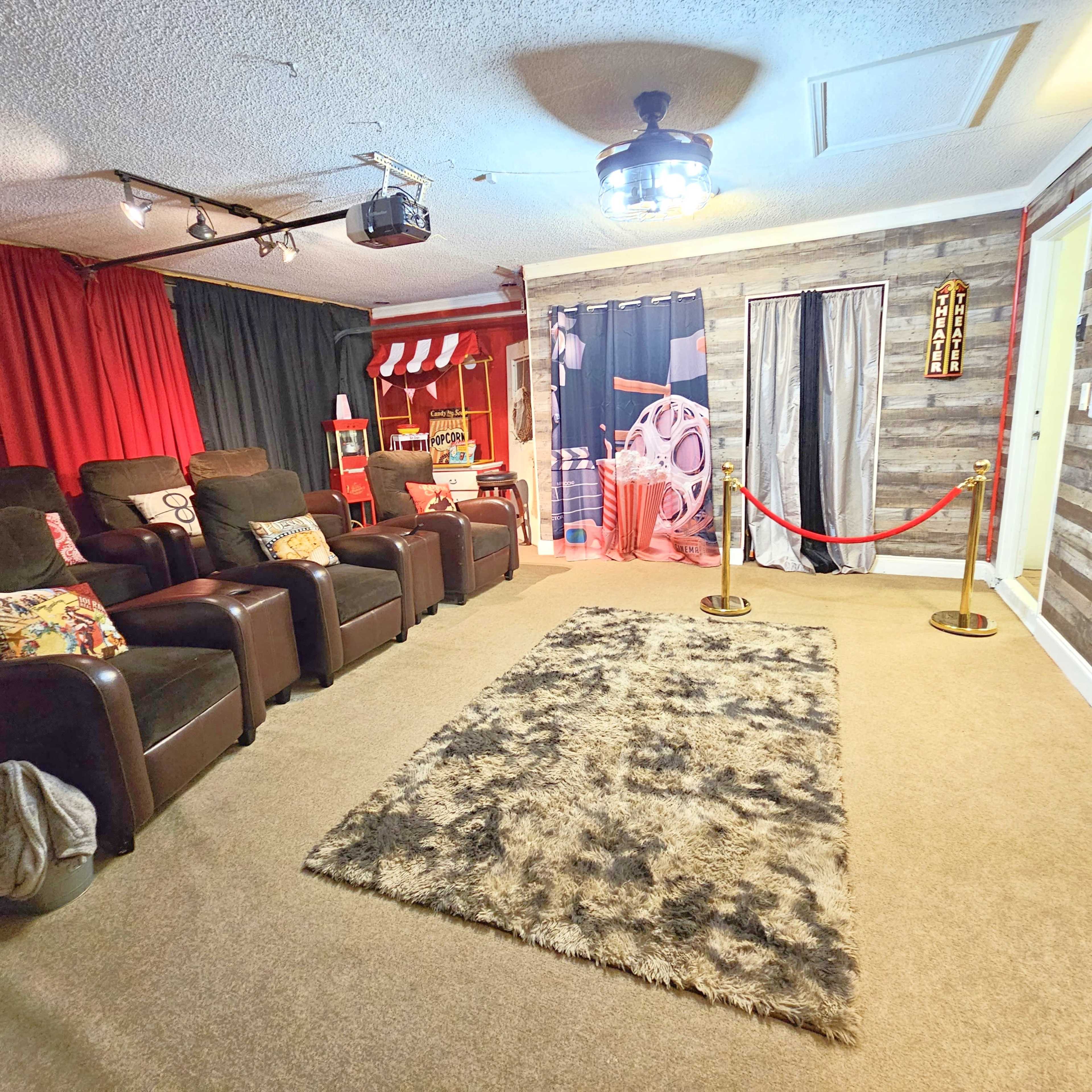 A cozy home theater setup with recliner chairs, a large area rug, and theatrical curtains, all illuminated by overhead lighting.