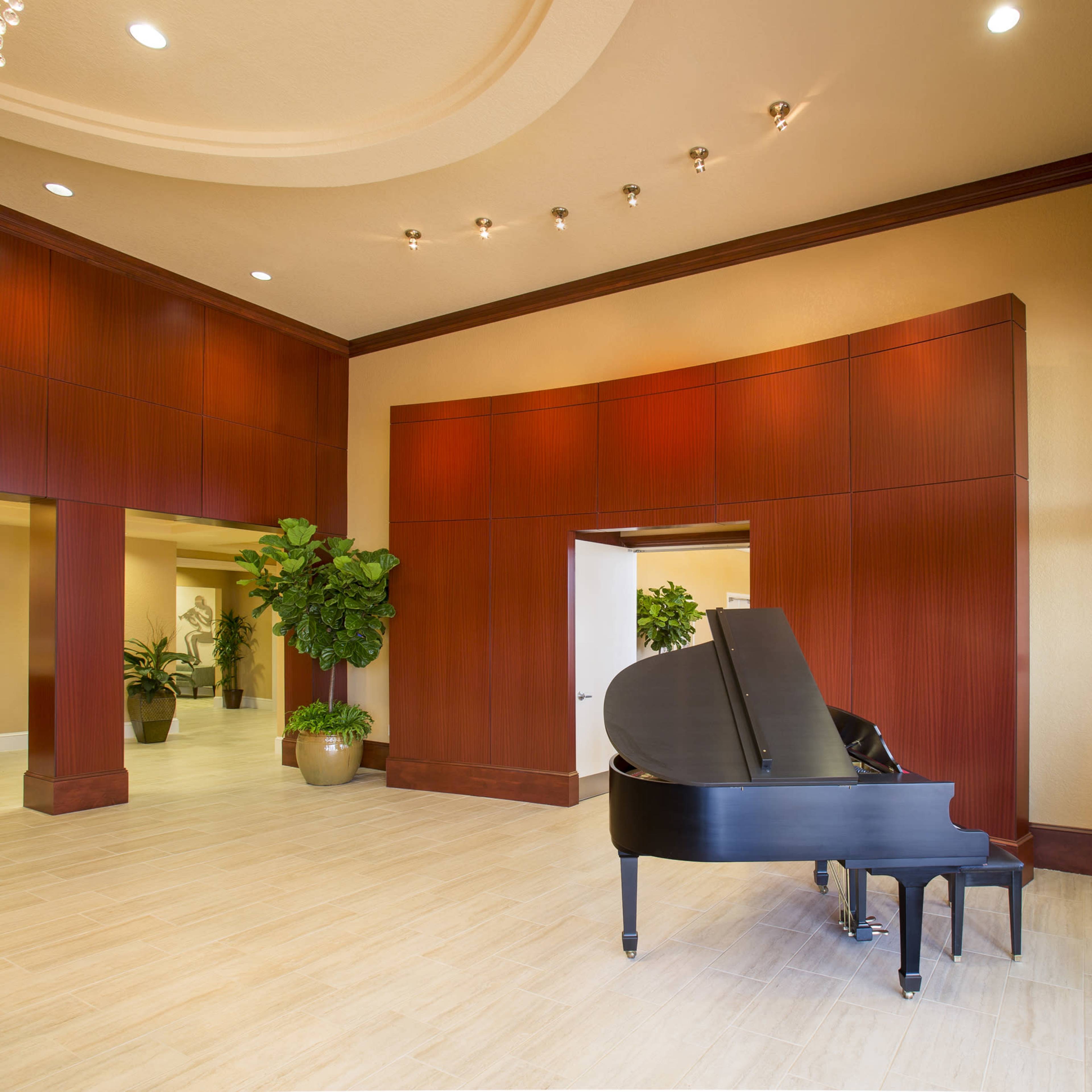 A spacious lobby featuring a black grand piano near a decorative chandelier and potted plants.