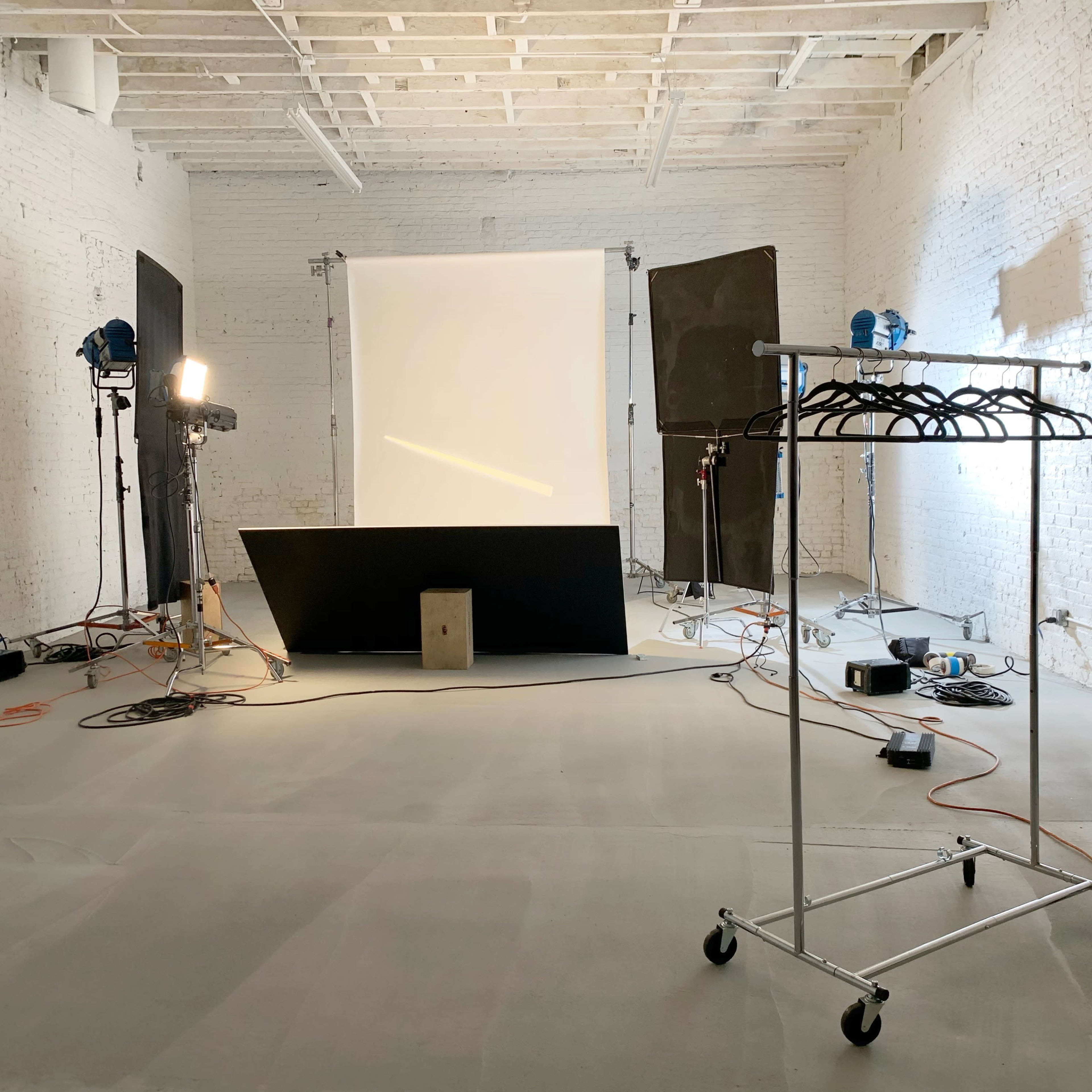 A photography studio with a light setup, backdrop, and a clothing rack on wheels.