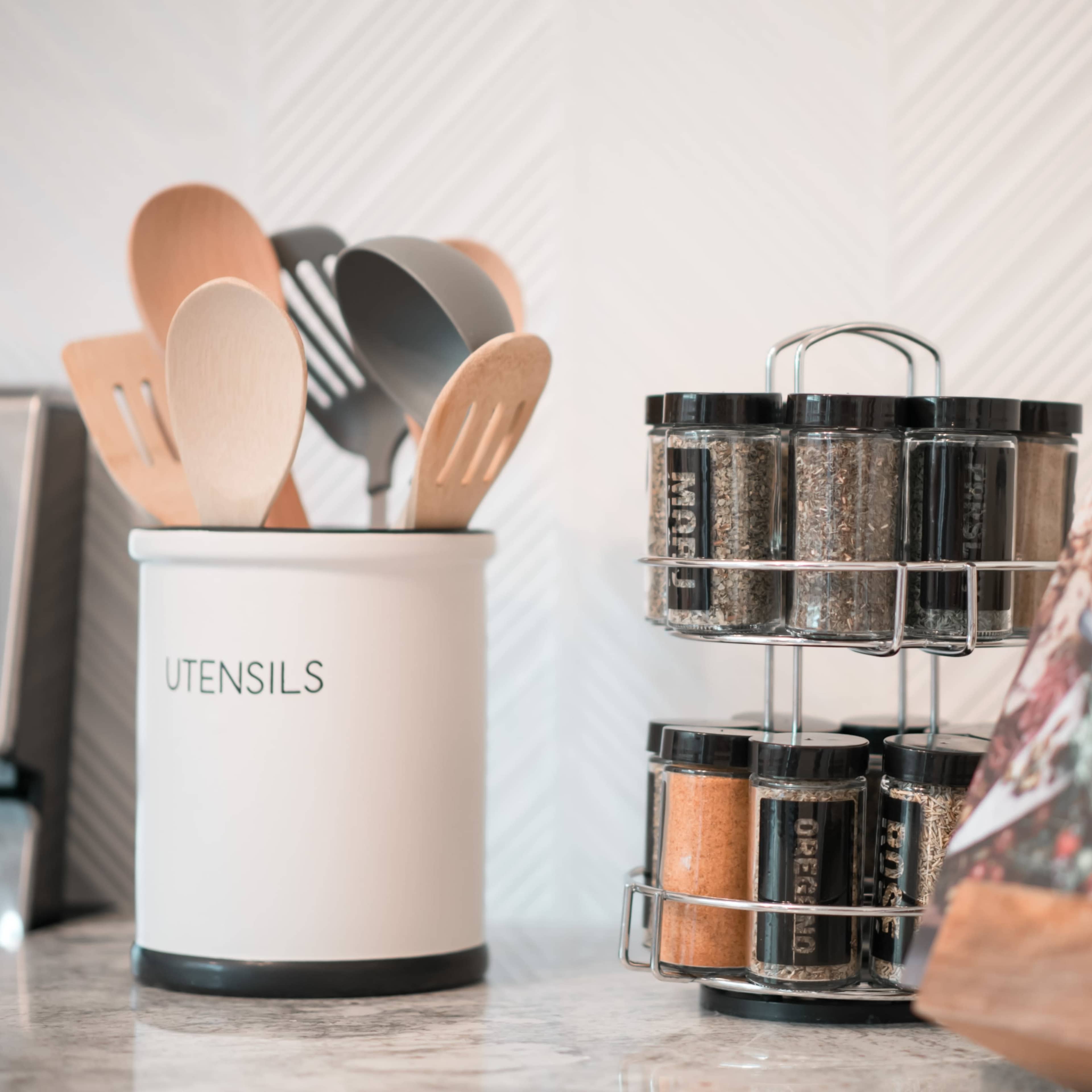 A kitchen countertop features a container labeled "UTENSILS," a tiered spice rack, and an open cookbook.