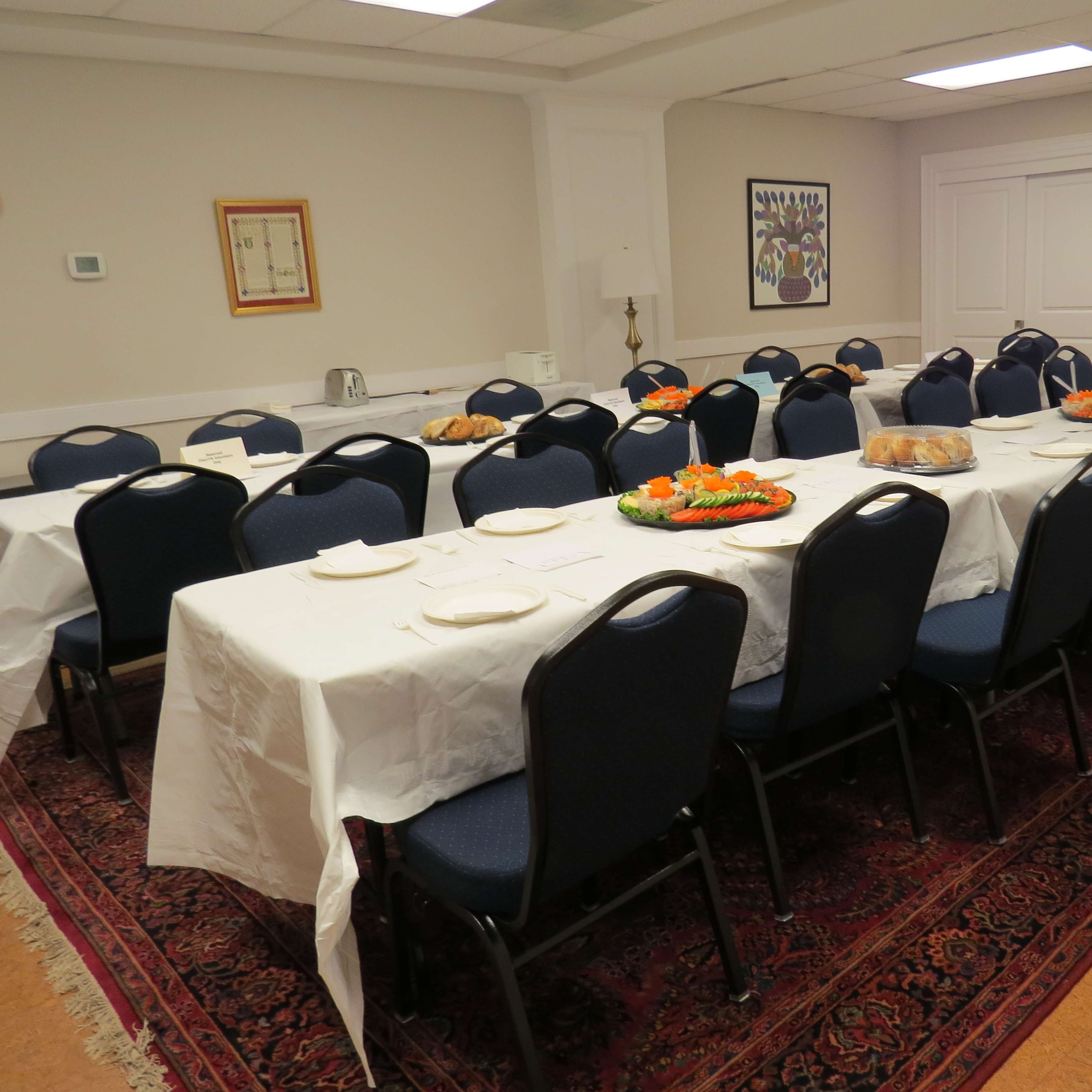 A long dining table is set with white tablecloths, plates, and food platters in a well-lit room.