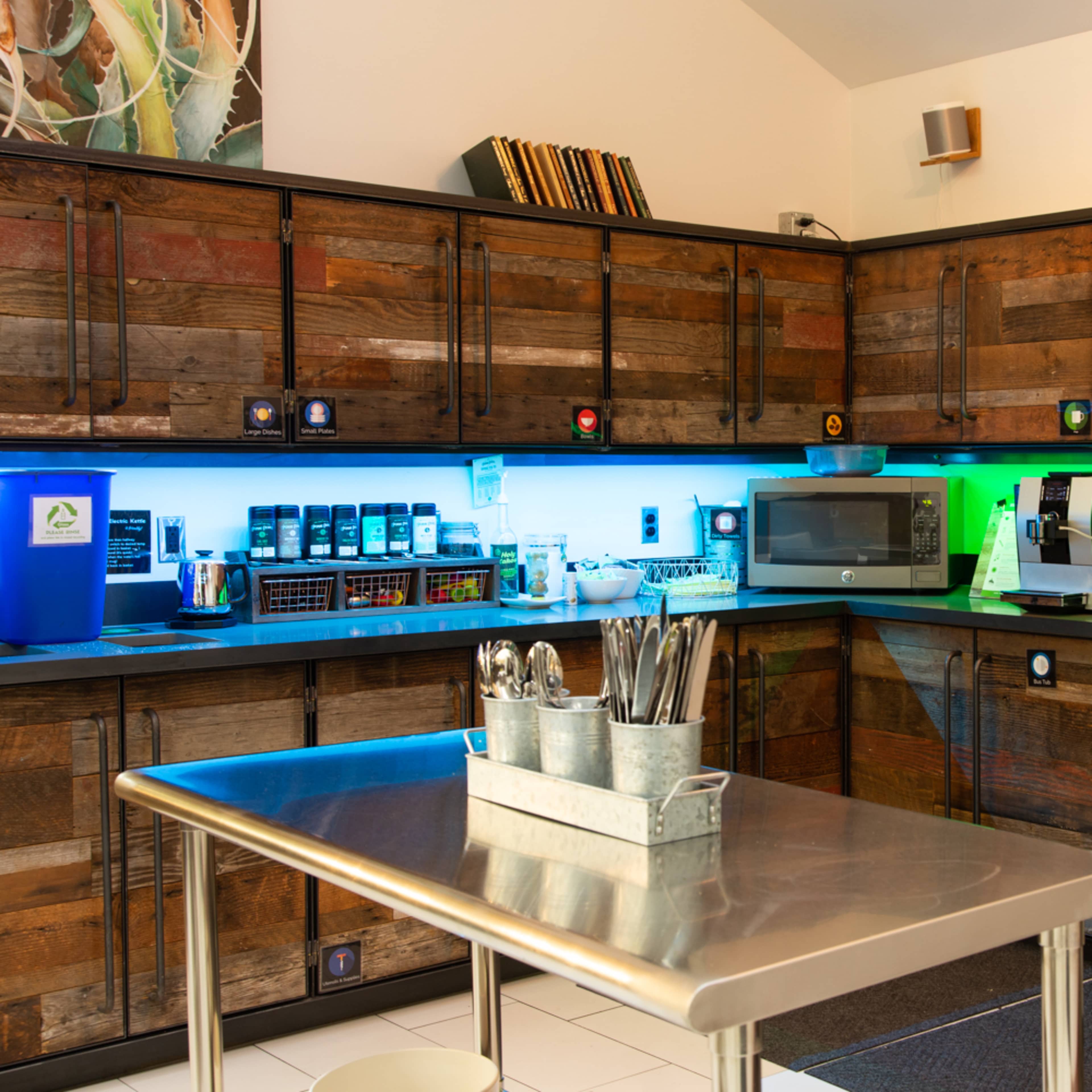 A modern kitchen with wooden cabinets, a stainless steel table, and colorful LED lighting under the cupboards.