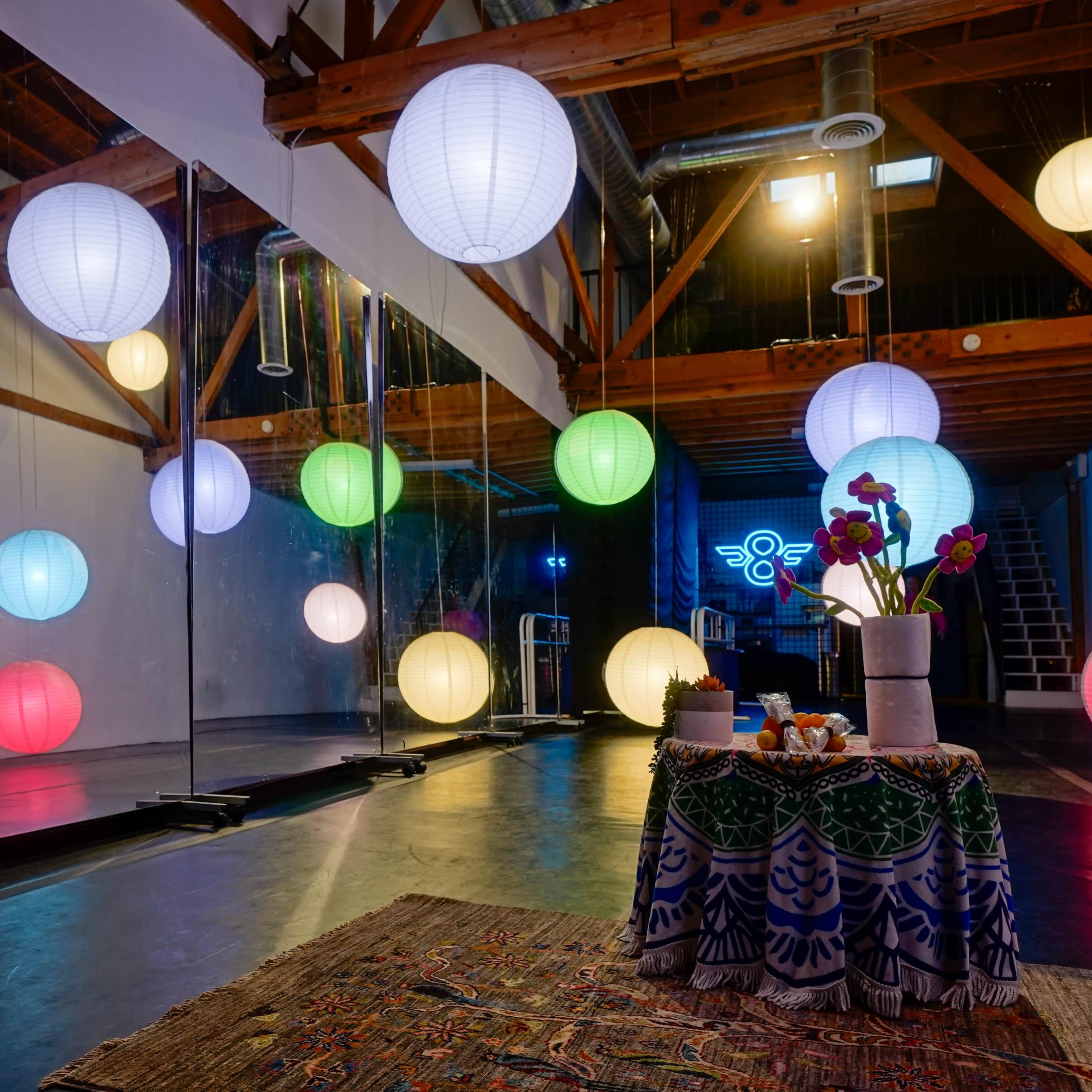 A spacious room features colorful hanging lanterns, mirrors, and a decorative table with flowers and items at its center.