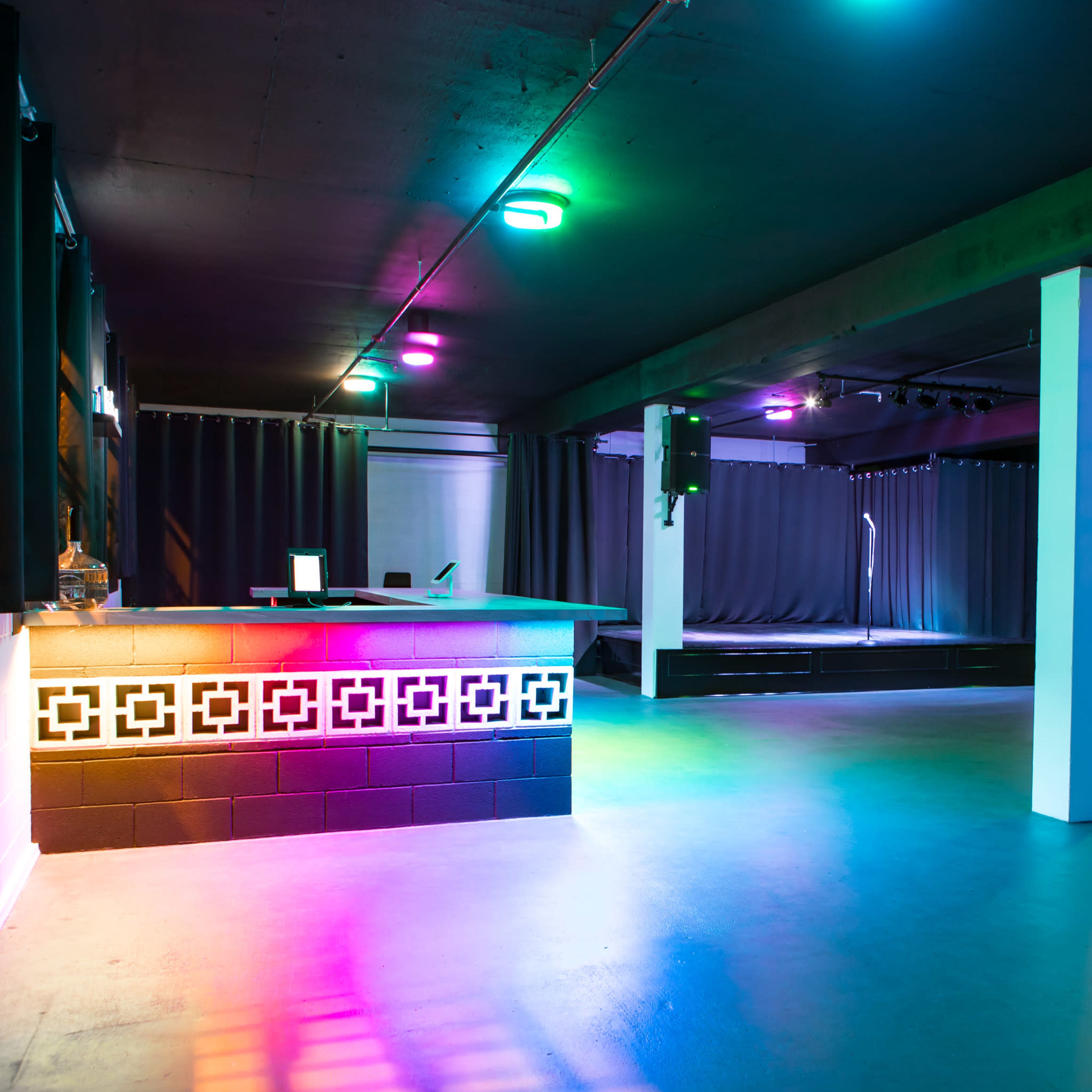 A dimly lit event space with a bar area, stage, and colorful lighting.