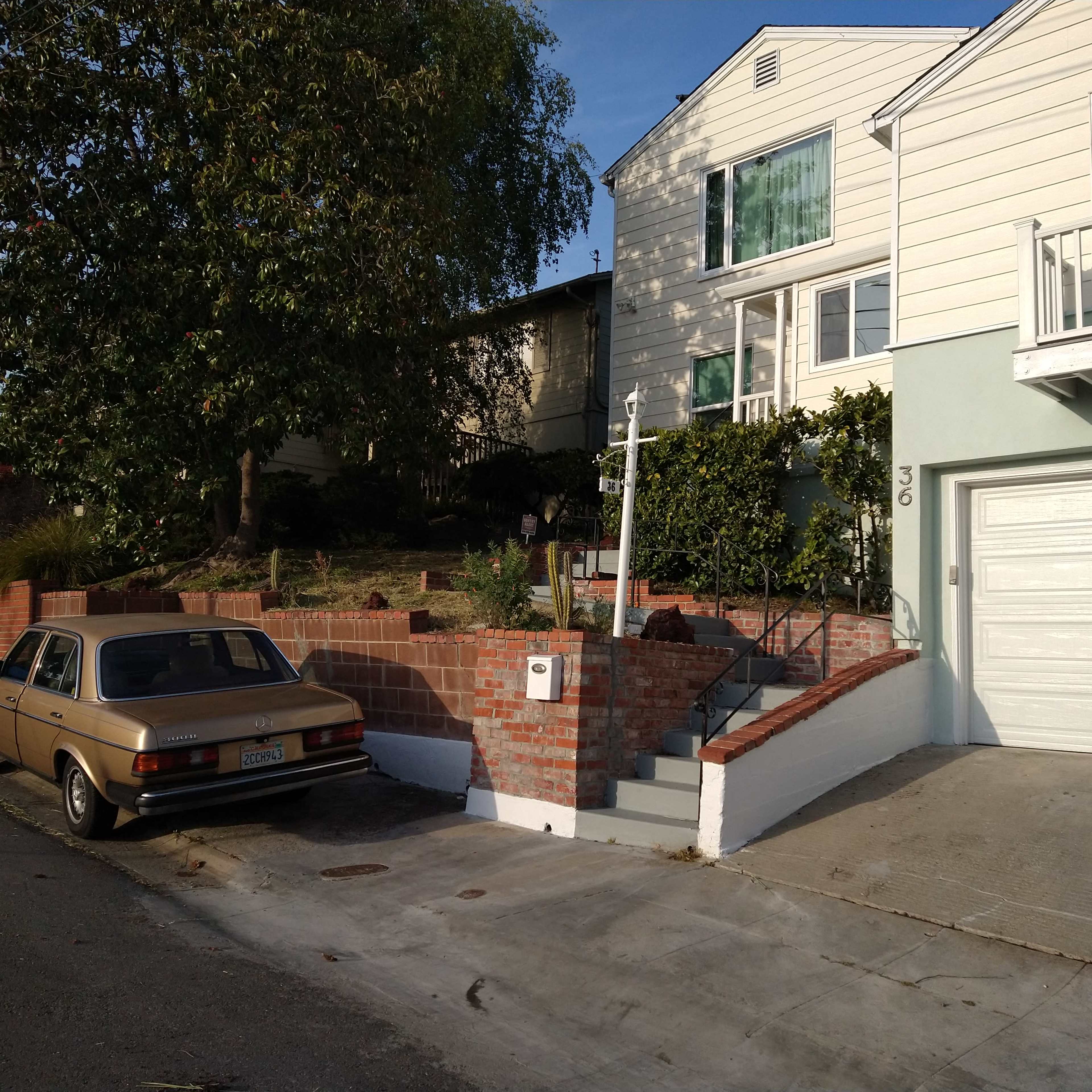 A vintage car is parked along the street next to a house with a two-car garage and landscaped steps leading to the front door.