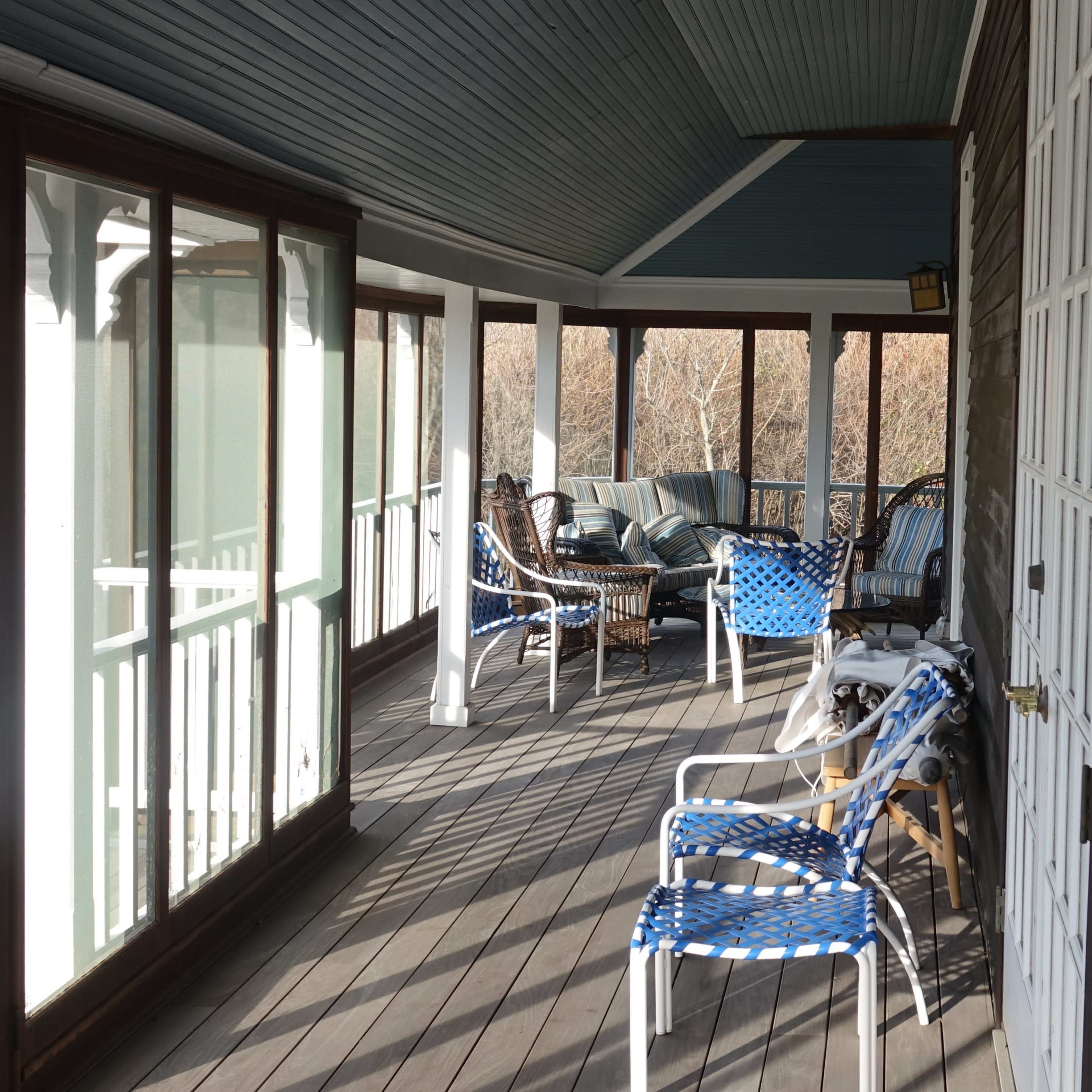 A covered porch with several chairs and tables arranged along the wooden floor.