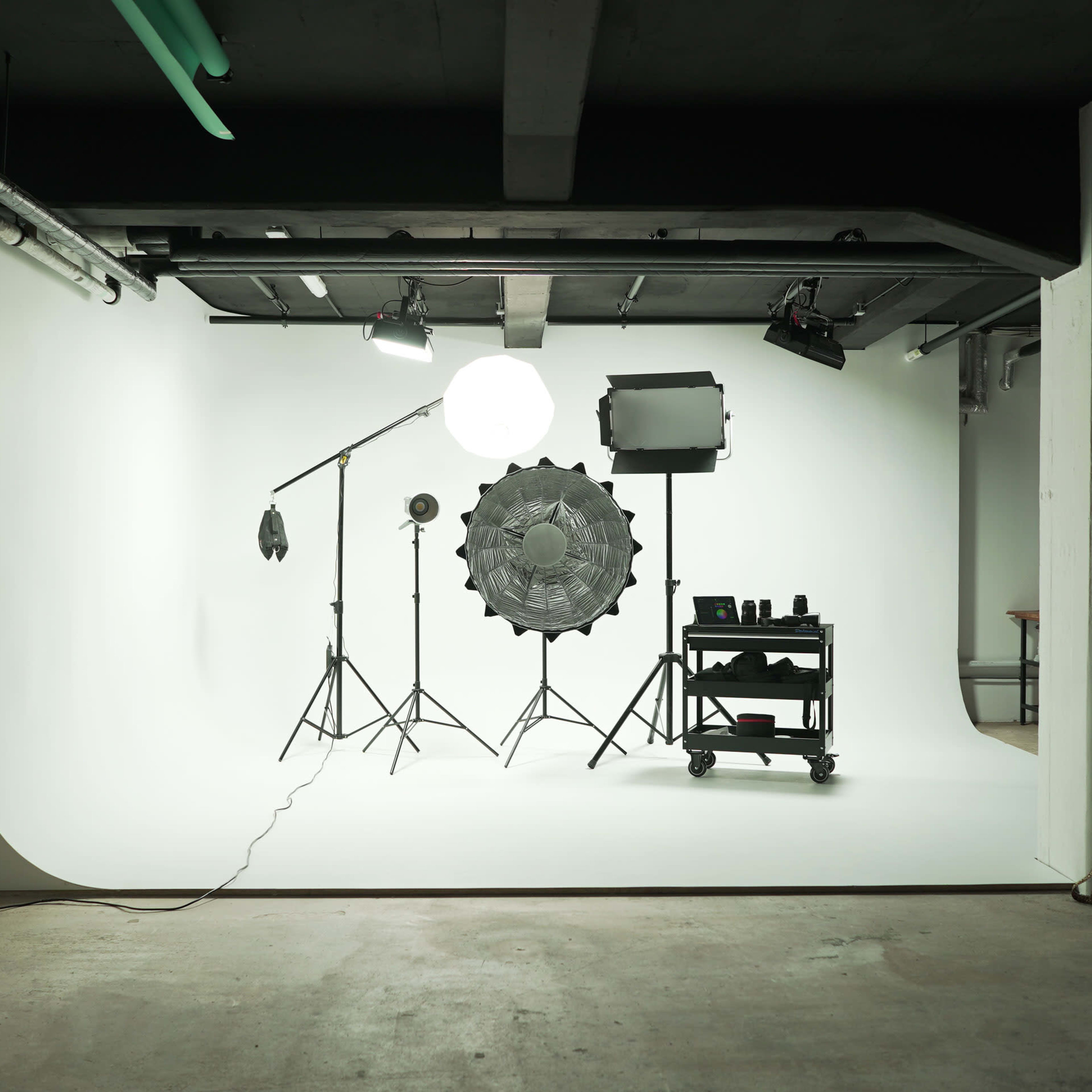 A photography studio setup featuring a backdrop, various lighting equipment, and a cart with photography accessories.