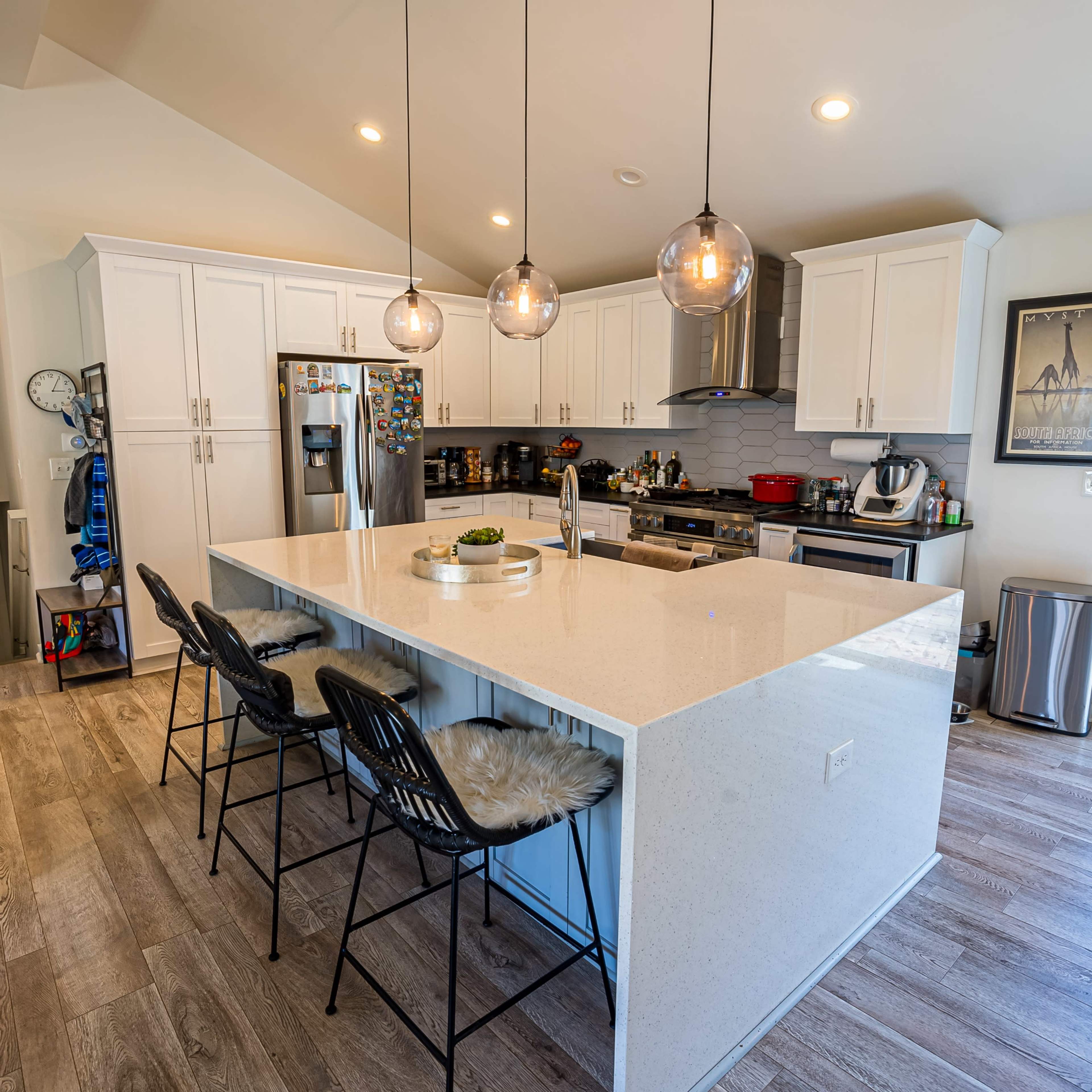 A modern kitchen features a large island with six chairs, stainless steel appliances, and white cabinetry.