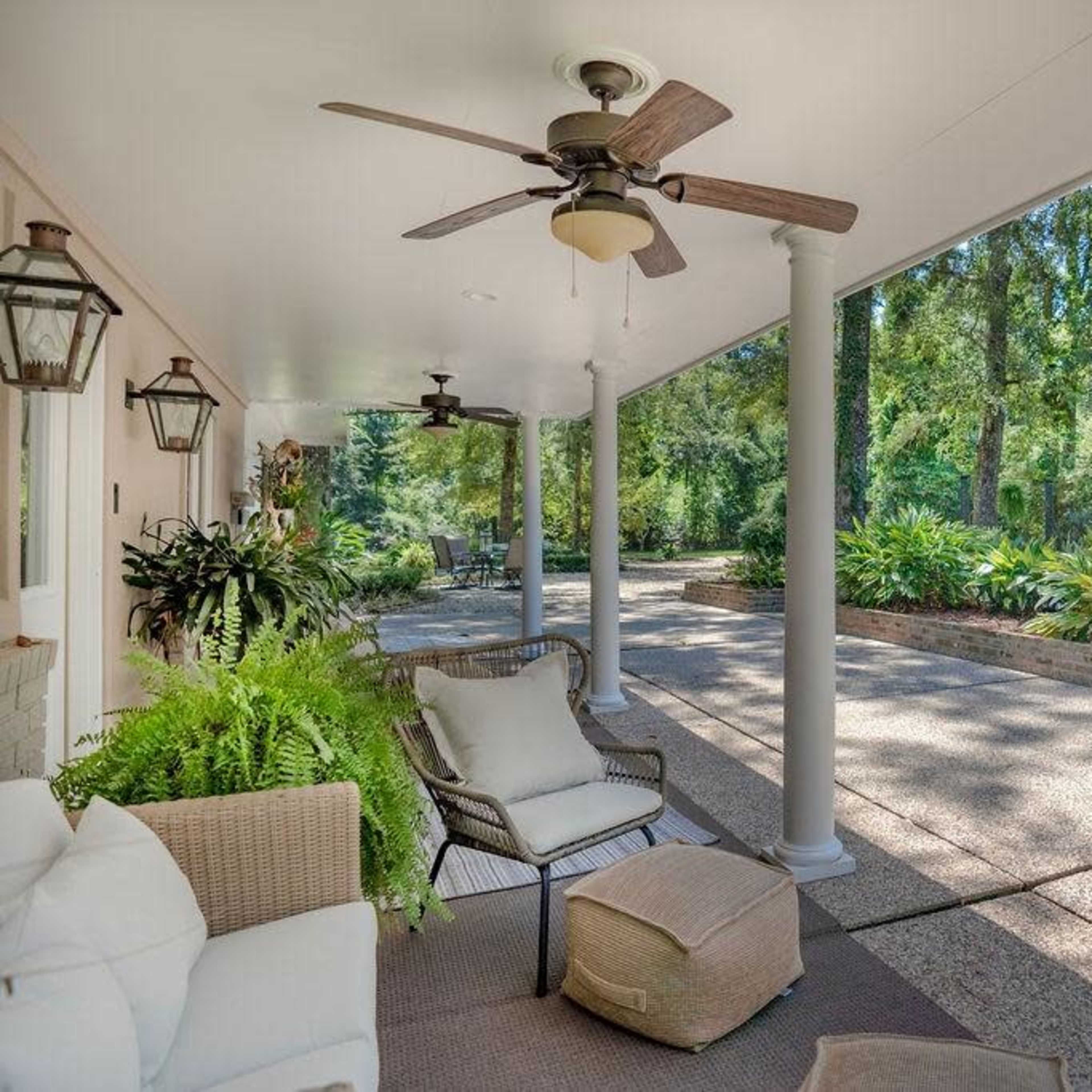 A covered porch features seating and decorative plants, surrounded by trees and a gravel path.
