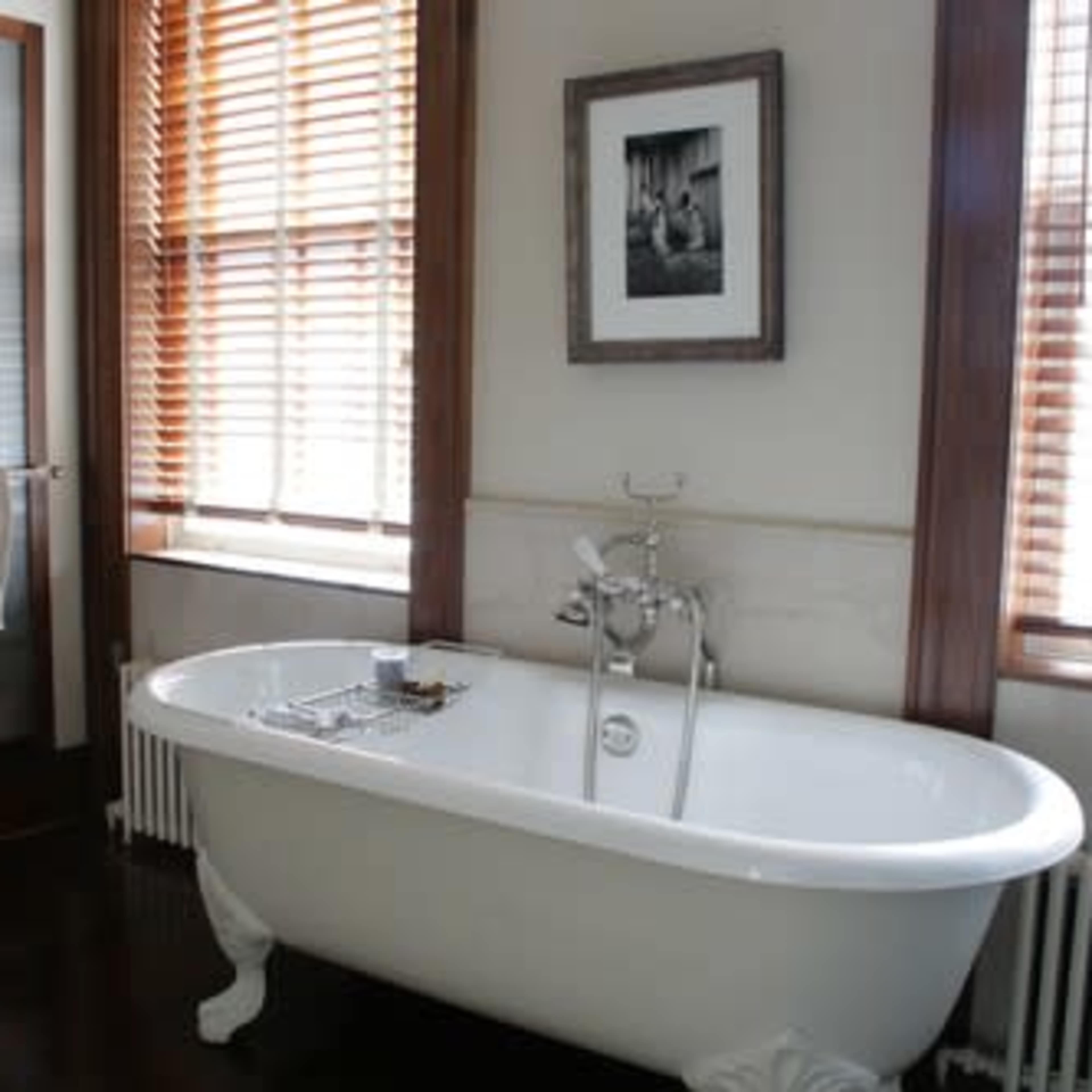 A bathroom featuring a freestanding white bathtub, a pedestal sink, and wooden blinds on the windows.