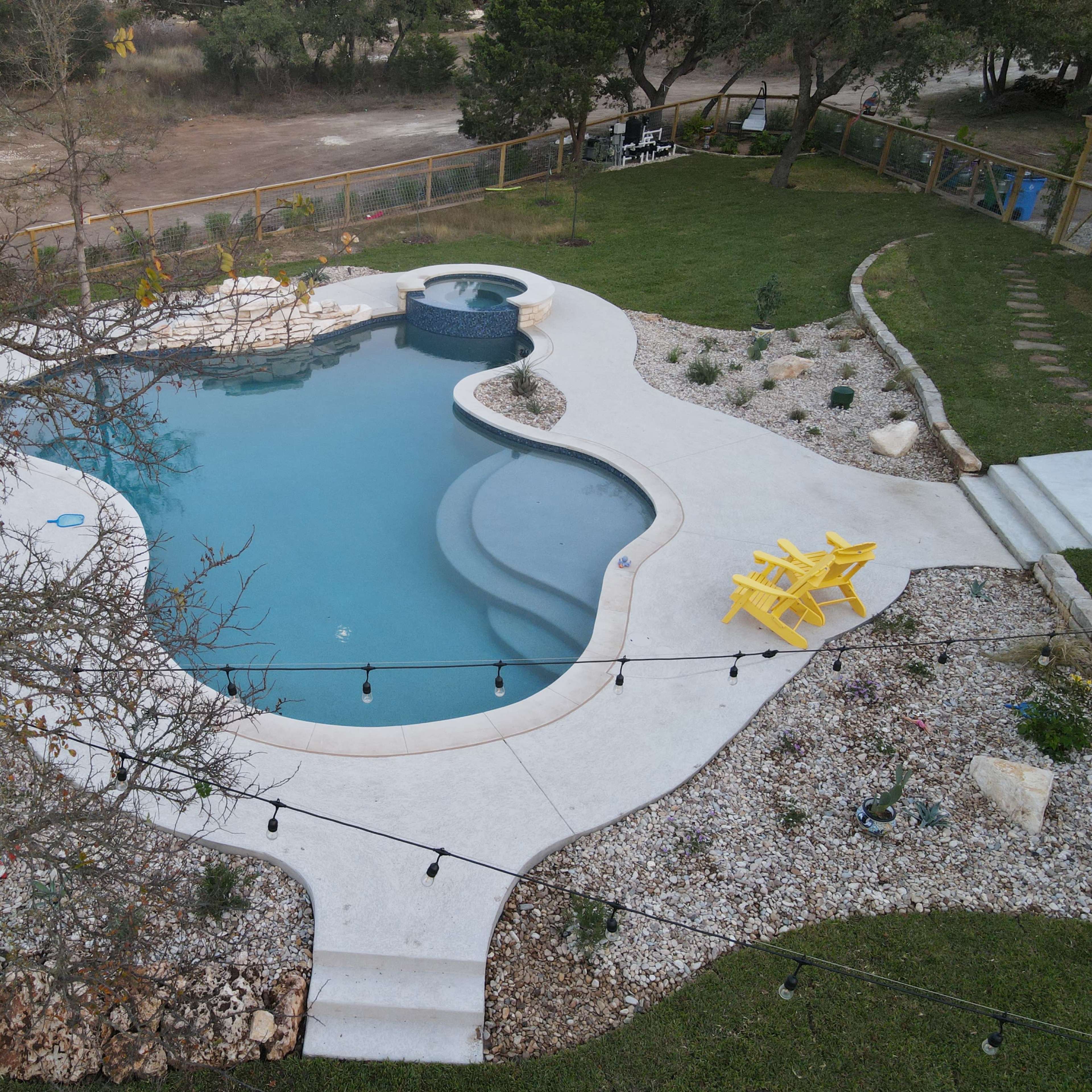 A rectangular swimming pool with a spa and surrounded by a landscaped area featuring rocks, plants, and two yellow chairs.
