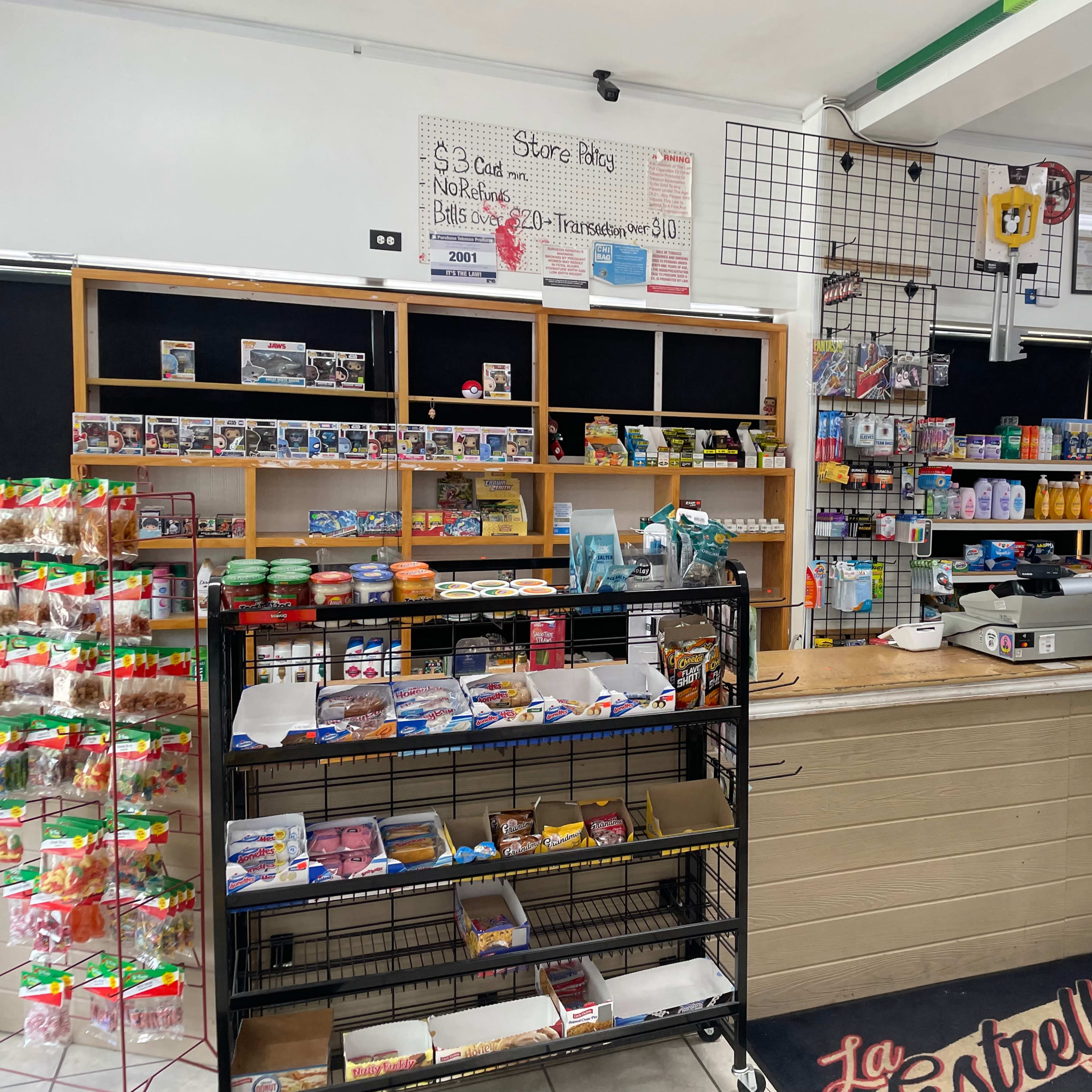 The interior of a small convenience store with shelves filled with snacks, beverages, and various products, alongside a checkout counter.