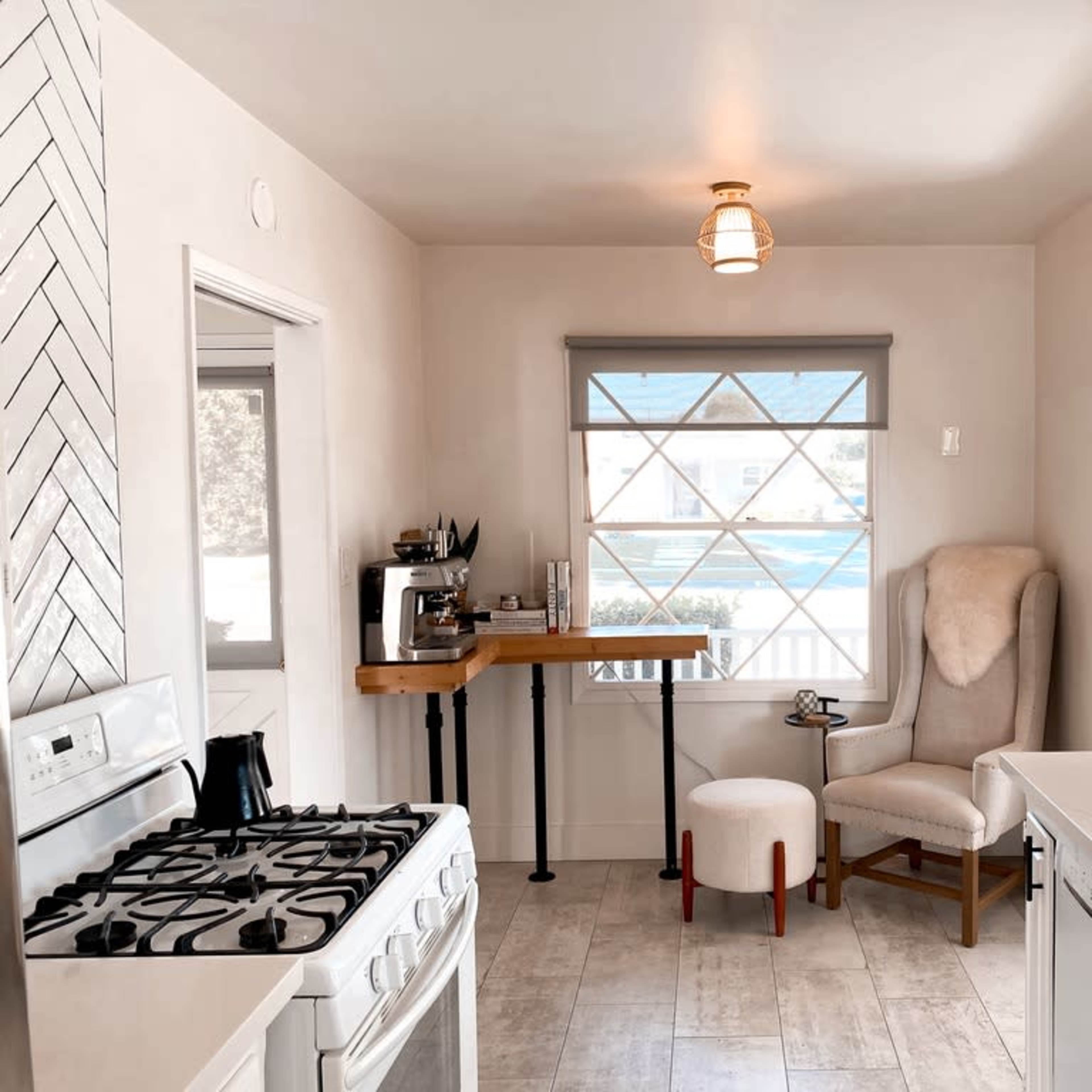 A bright kitchen featuring a gas stove, a small dining area with a tall table and a chair, and a large window with a view.