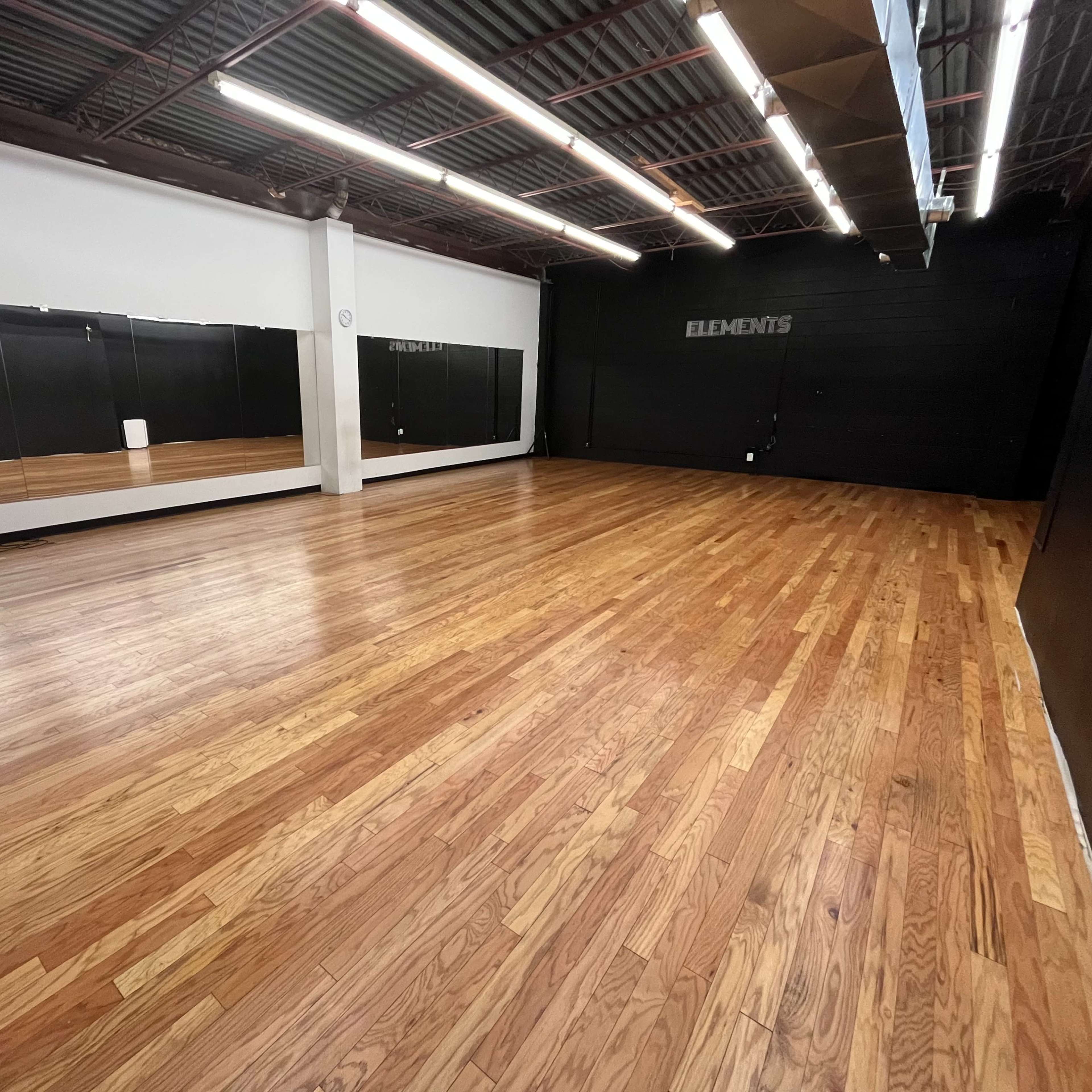 An empty dance studio with wooden flooring and mirrors on one wall.