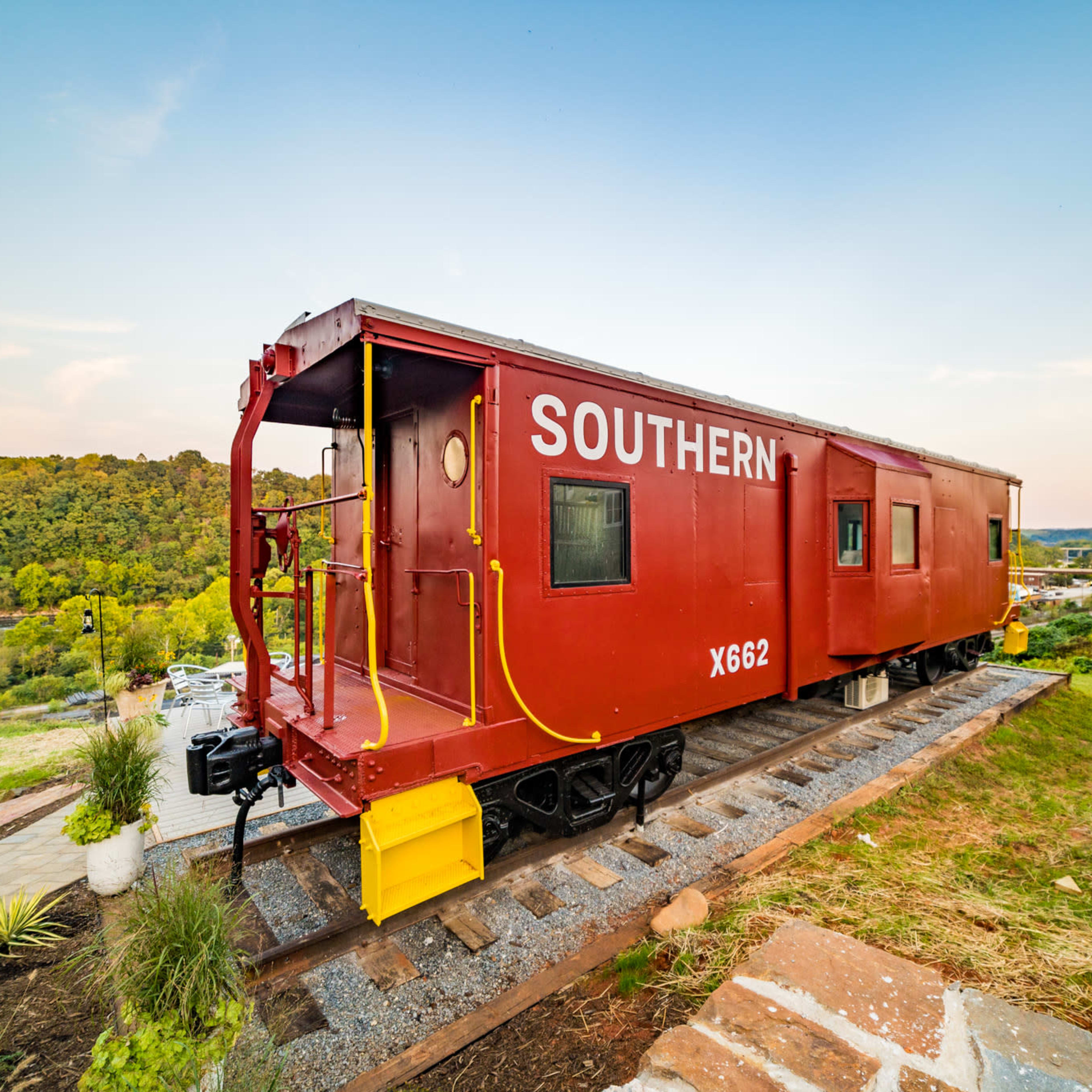 A red caboose labeled "SOUTHERN X662" is positioned on a set of tracks overlooking a green landscape and river.