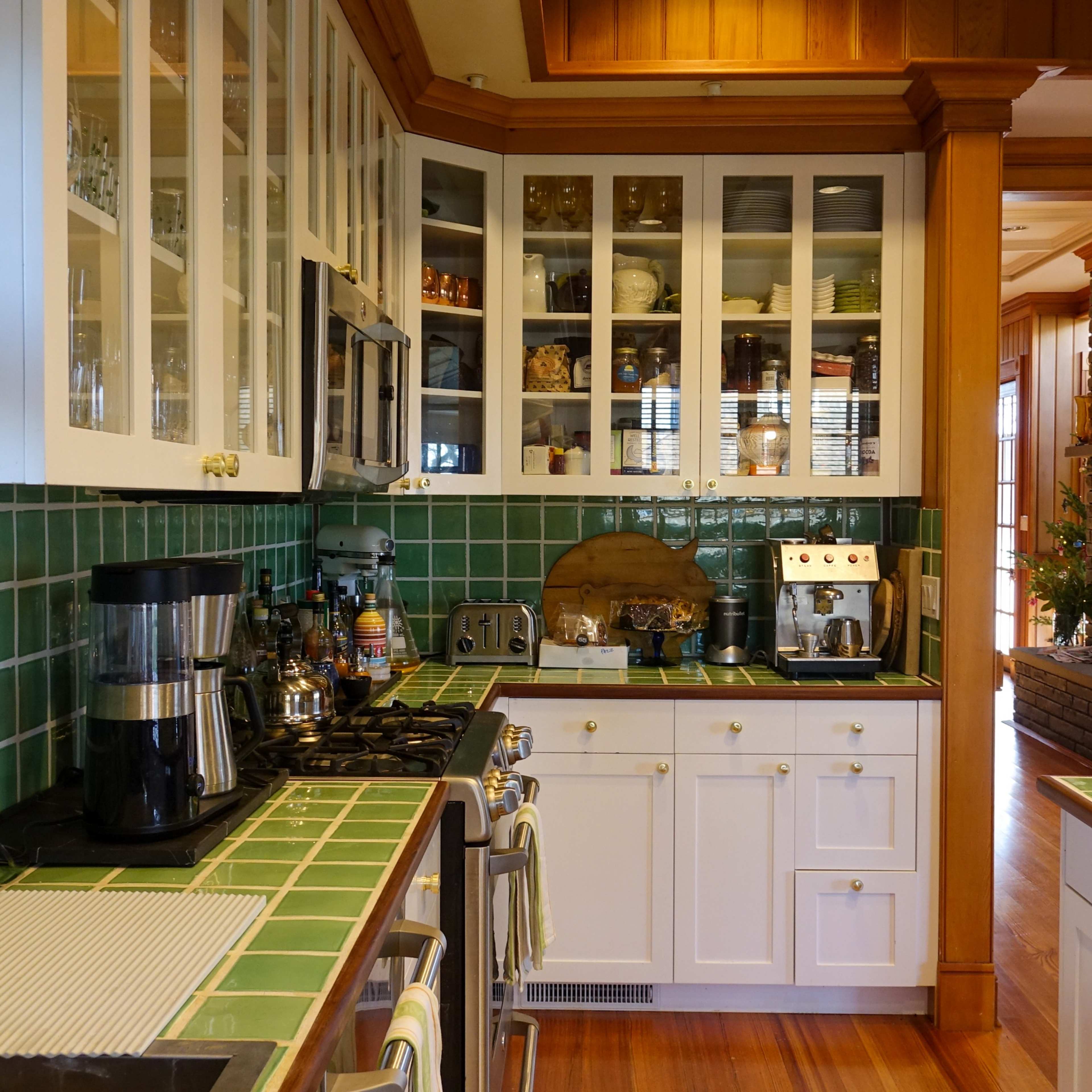 A kitchen featuring green tiled countertops, white cabinets with glass doors, and various kitchen appliances.