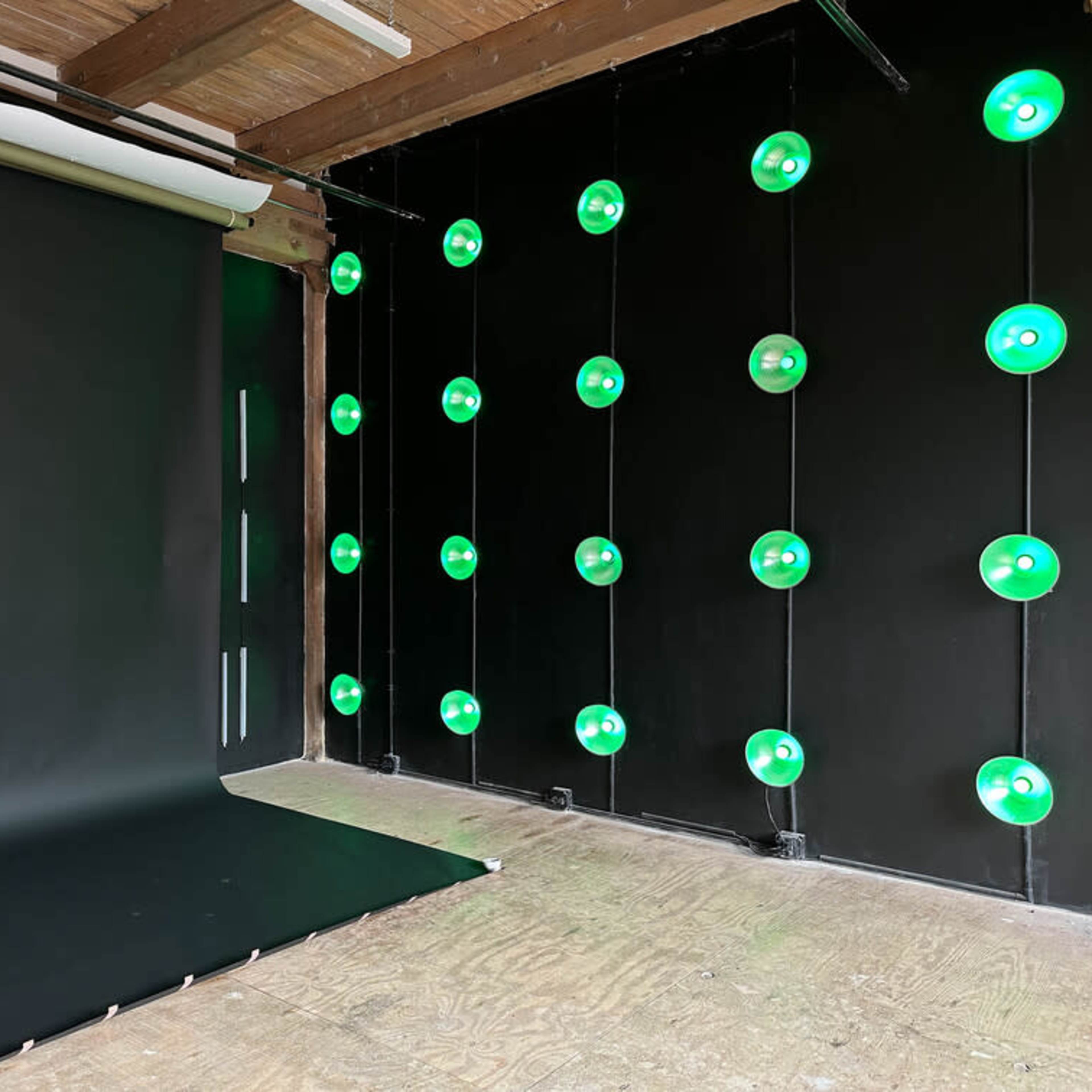 A photography studio features a black backdrop and floor, with green lights mounted on the walls.
