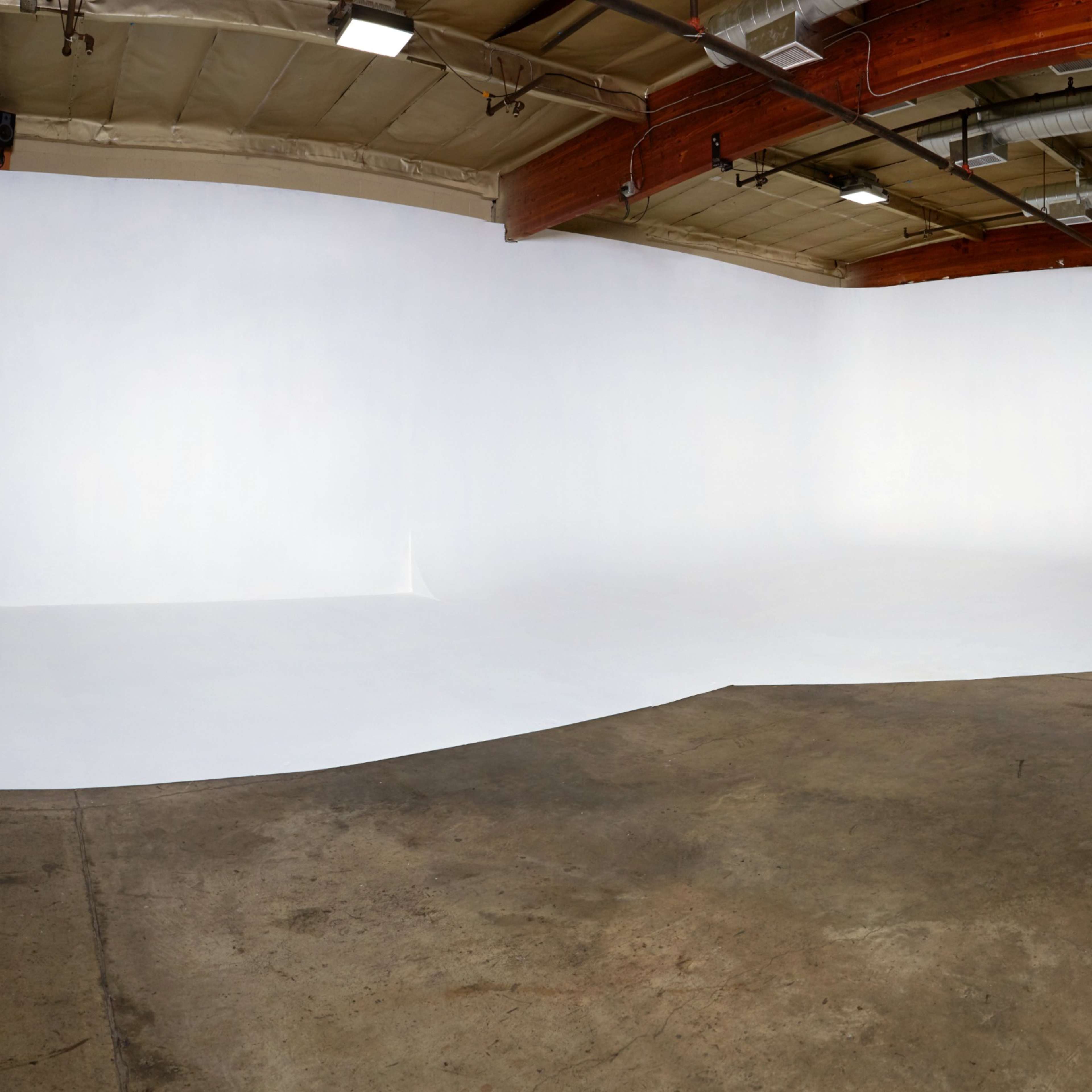 A spacious photo studio with a seamless white backdrop and a concrete floor.