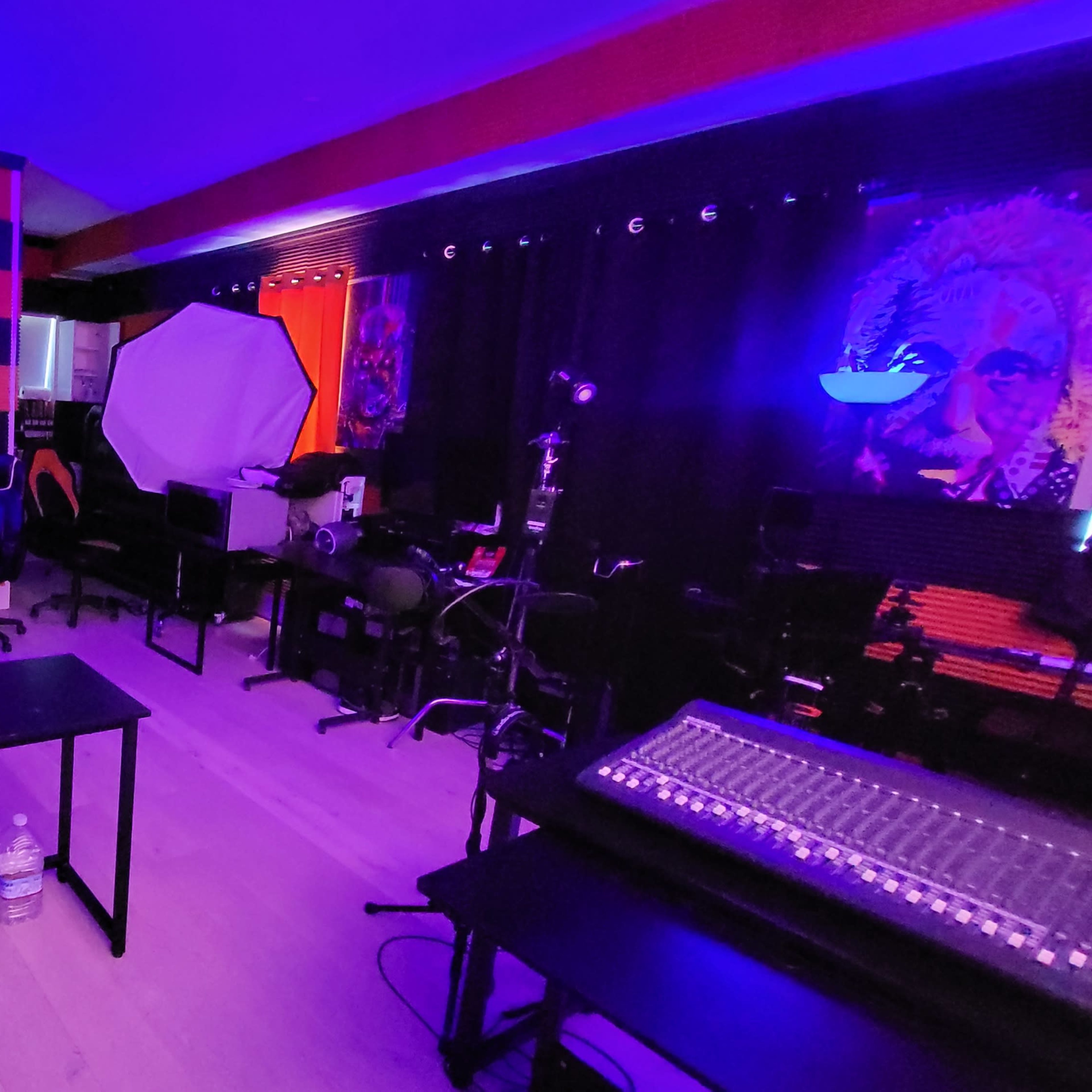 A dimly lit recording studio with two large softboxes, various musical equipment, and chairs arranged around a central table.