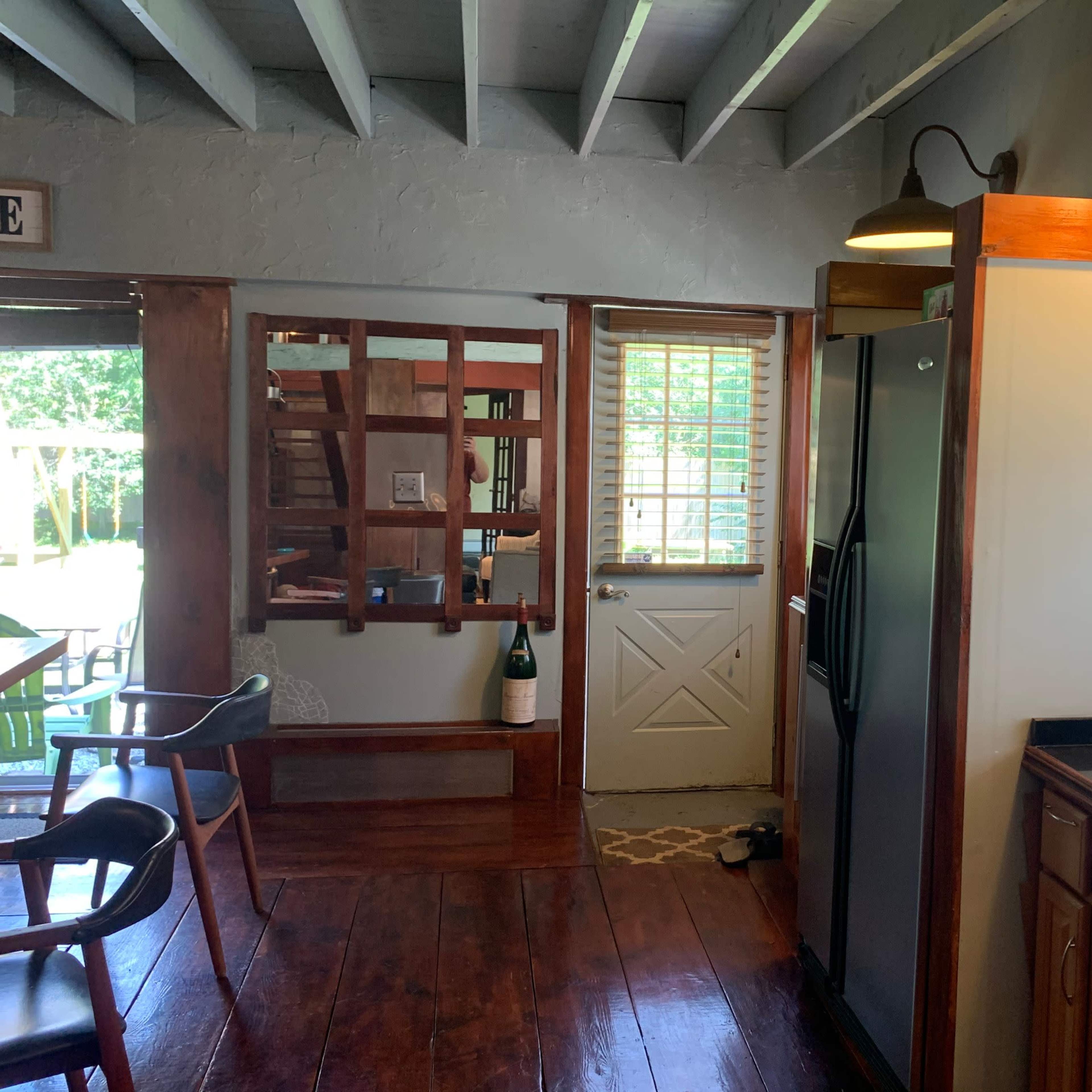 A kitchen with wooden cabinets, a stainless steel refrigerator, and a door leading outside, alongside visible furniture and a watermelon on the counter.