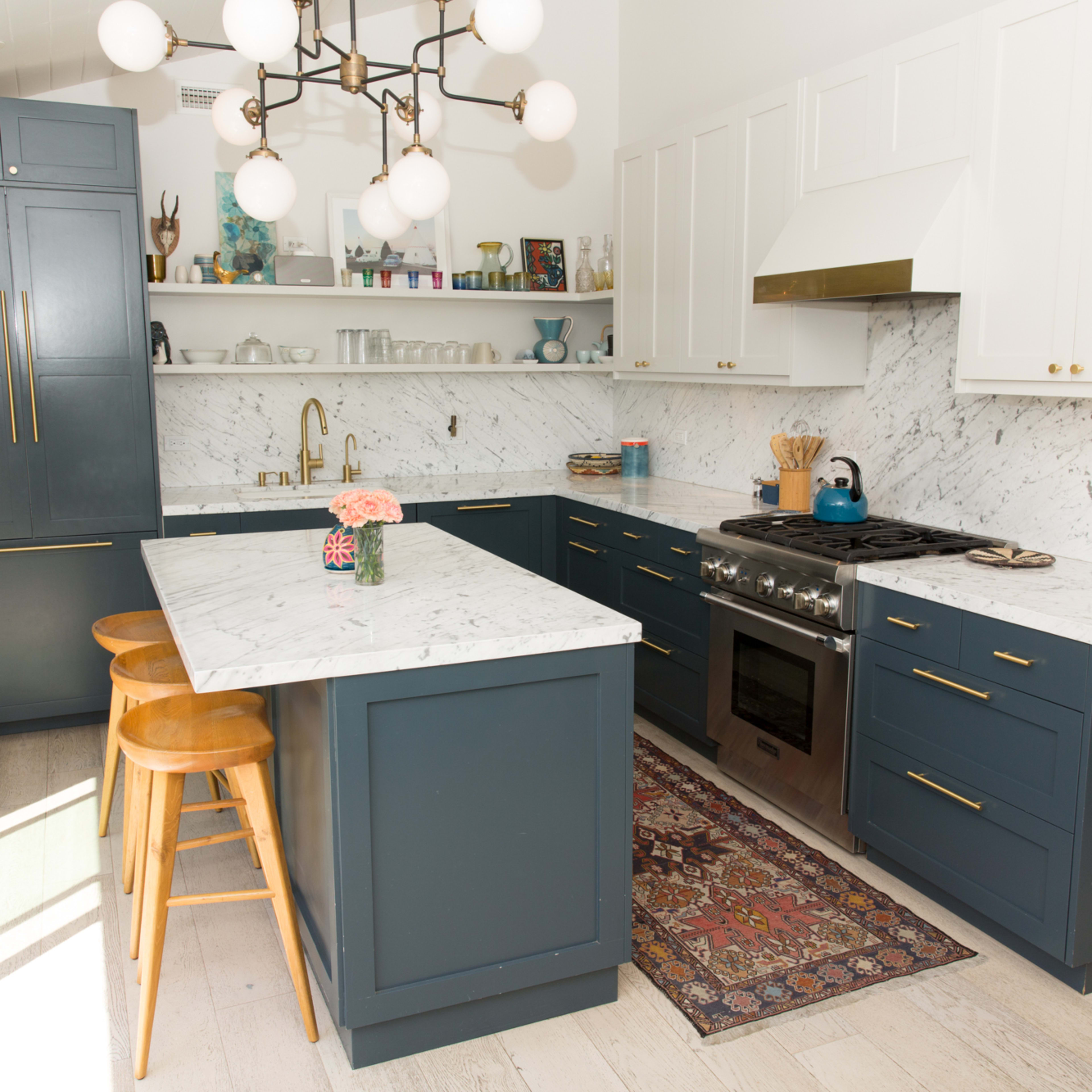 A modern kitchen with navy blue cabinetry, a marble countertop, and an arranged layout featuring a stove, sink, and wooden bar stools.