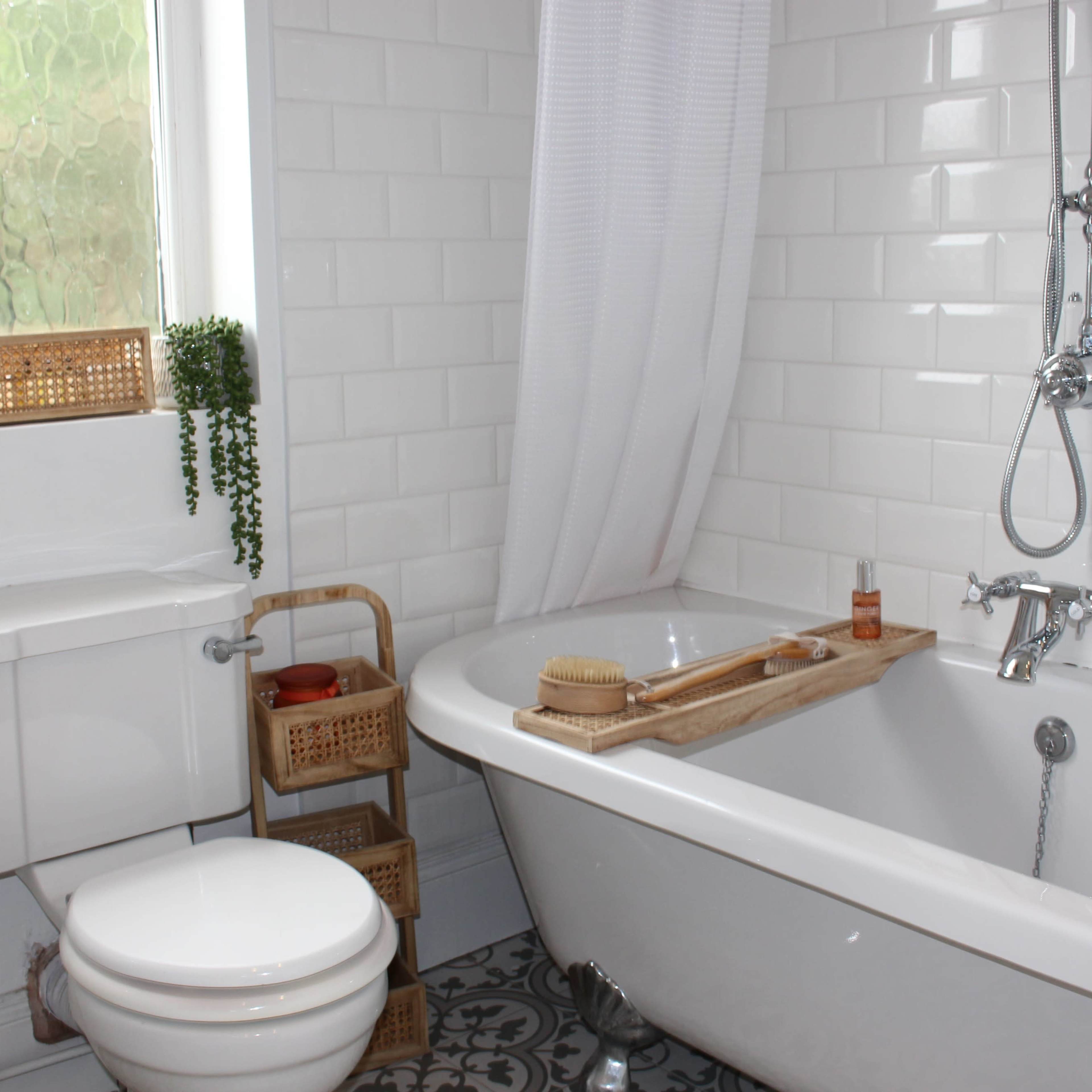 A bright bathroom features a freestanding bathtub, a showerhead, a toilet, and a wooden tray with bath accessories.