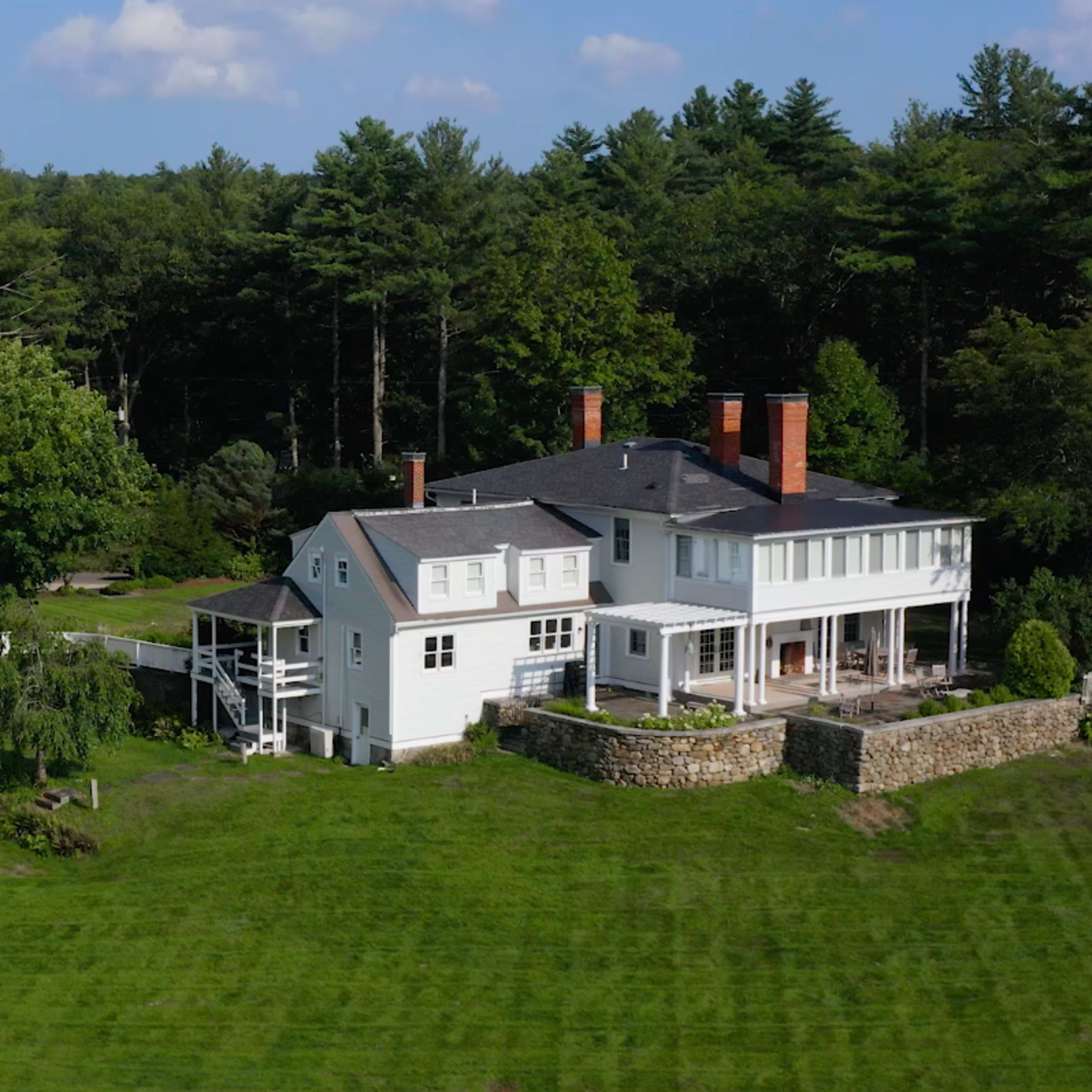 A large property featuring a modern white house and a separate garage or workshop surrounded by green grass and trees.
