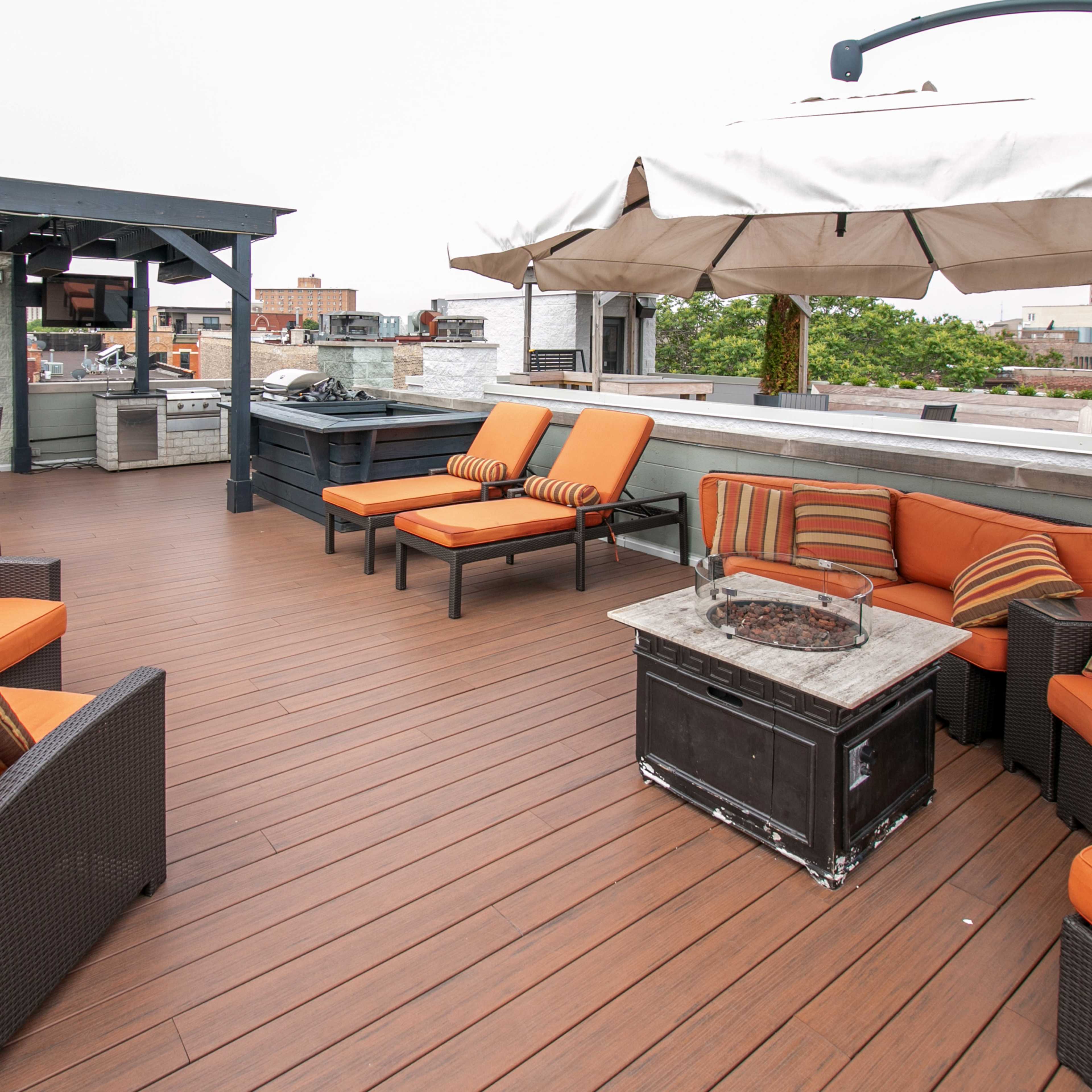 The rooftop terrace features a seating area with orange cushions, a fire pit table, and an outdoor kitchen sheltered by a pergola.