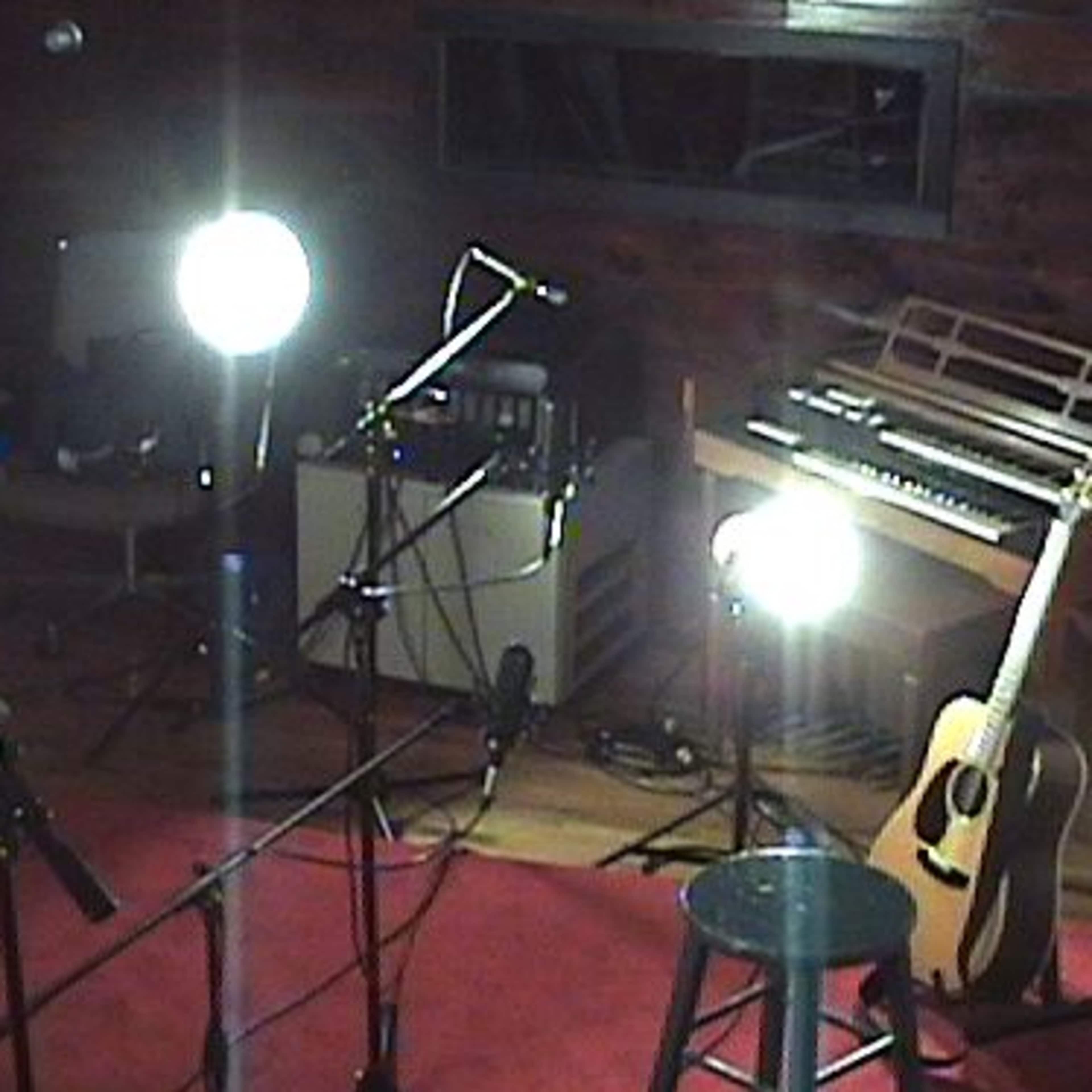 A recording studio setup with studio lights, microphones, and an acoustic guitar placed next to a stool.