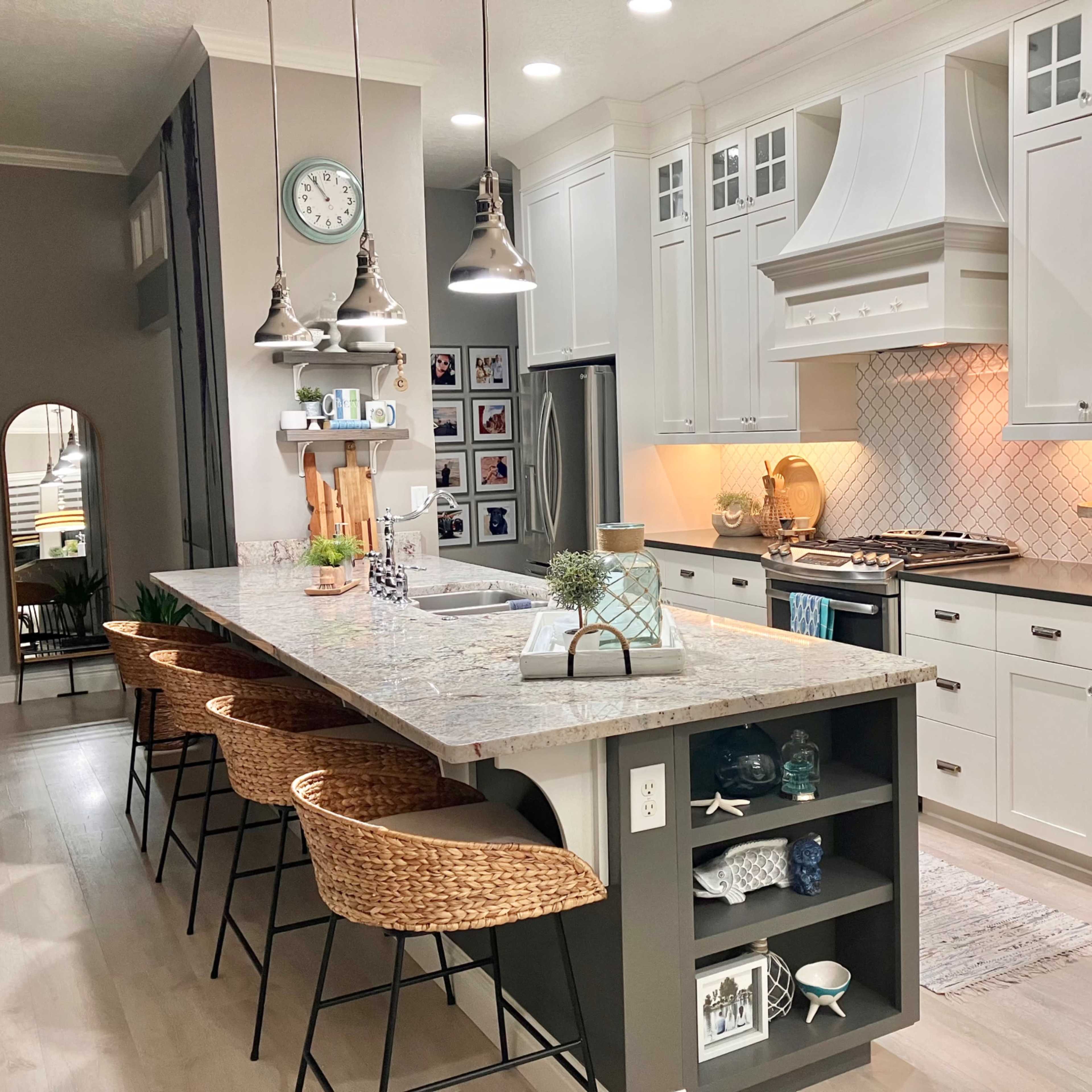 A modern kitchen features white cabinetry, a large island with bar stools, and stainless steel appliances, highlighted by warm lighting and decorative accents.
