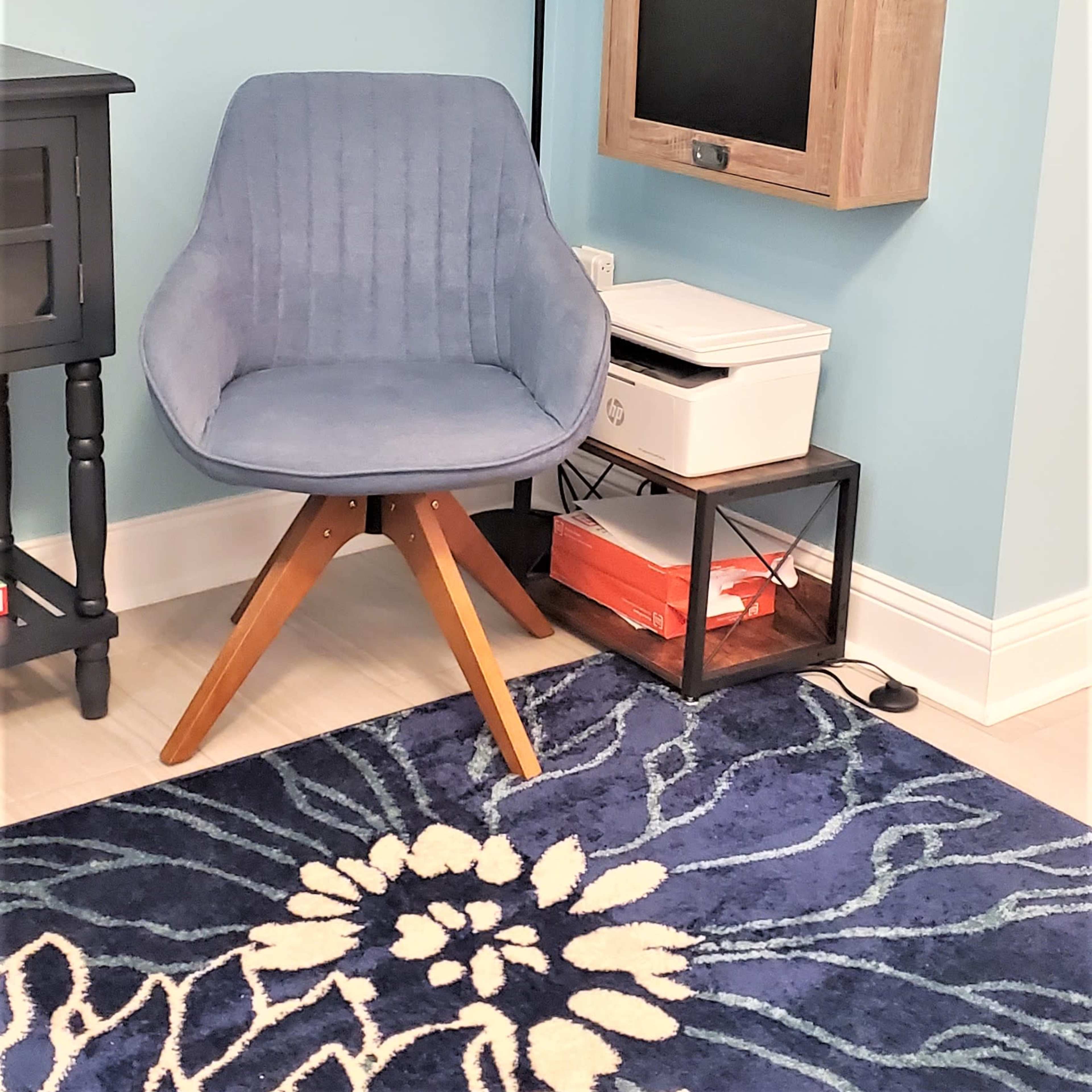 A light blue room with a blue chair, a wall-mounted blackboard, a floor lamp, and a decorative rug.