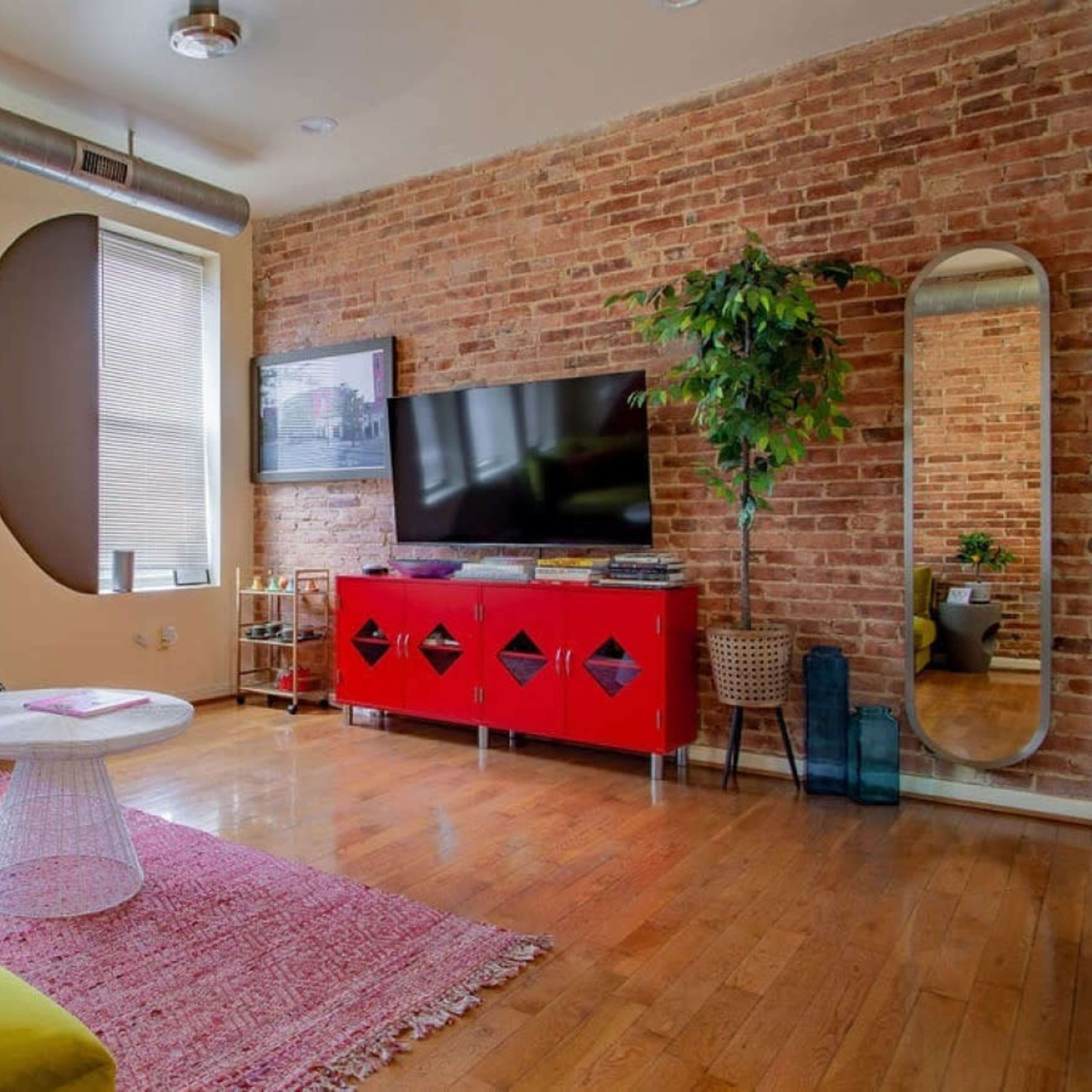A stylish living room featuring a brick wall, a green sofa, a circular coffee table, and a red TV stand with decorative elements.